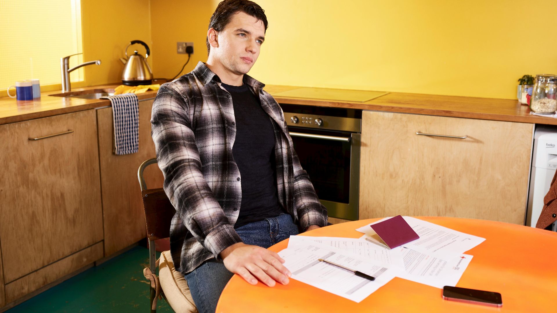 Man sitting at a kitchen table with documents and a passport, contemplating.