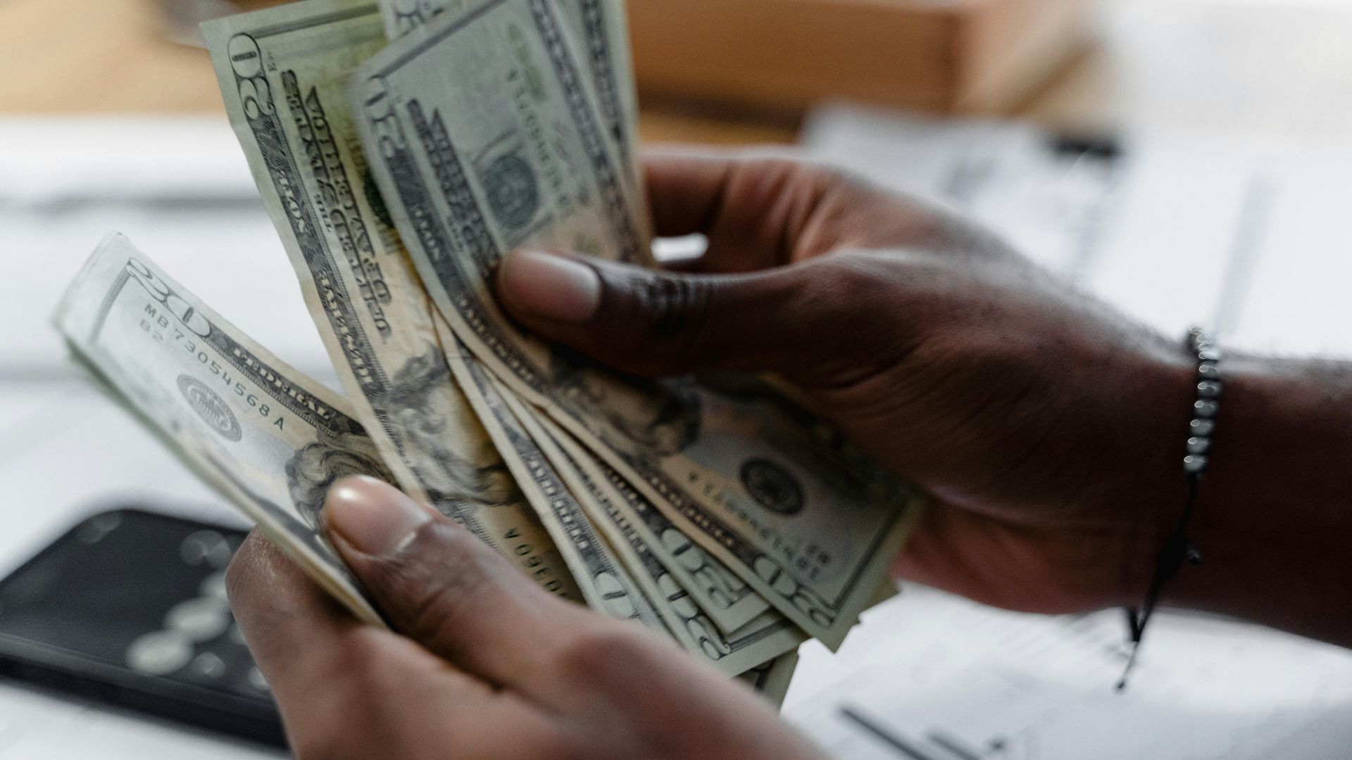 Detailed image of hands counting US dollar bills on a desk, emphasizing finance and budgeting.