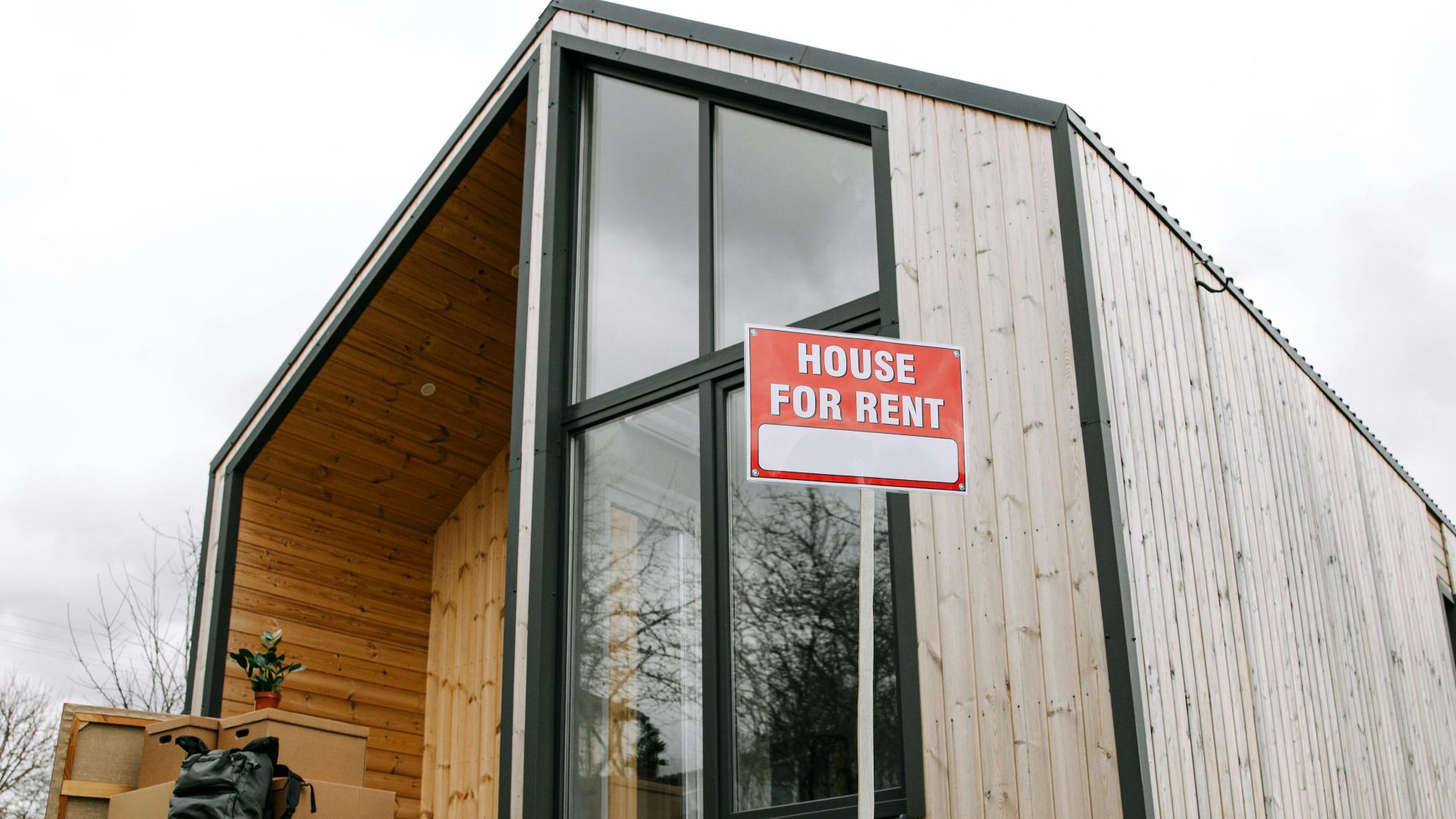 Low-angle view of a modern wooden house with a 'House for Rent' sign, showcasing contemporary architecture.