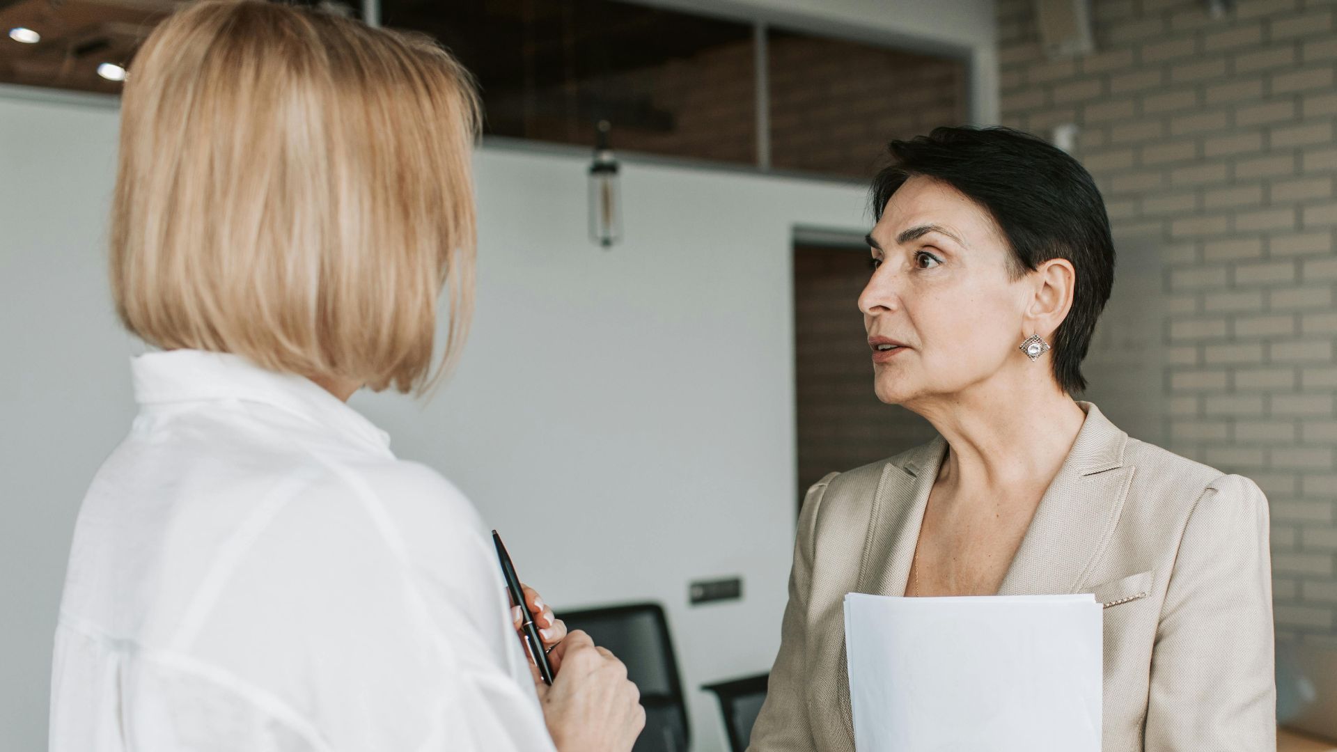 Two businesswomen engage in a conversation during a professional meeting in a modern office.