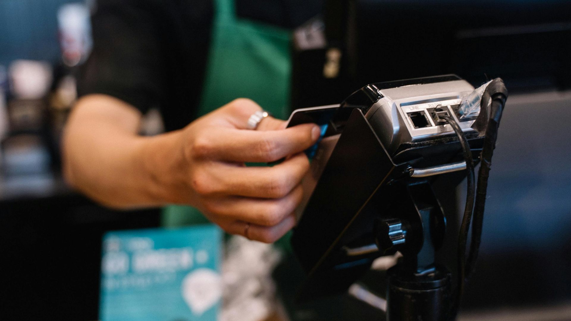 Close-up of a barista processing a payment using a card reader in a café setting.