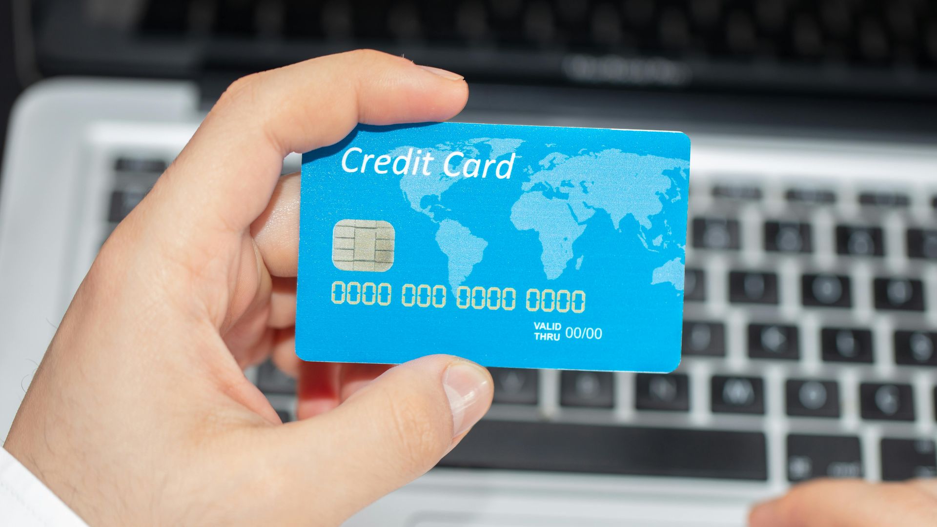 Person holding credit card near laptop for online shopping, emphasizing secure online transactions.