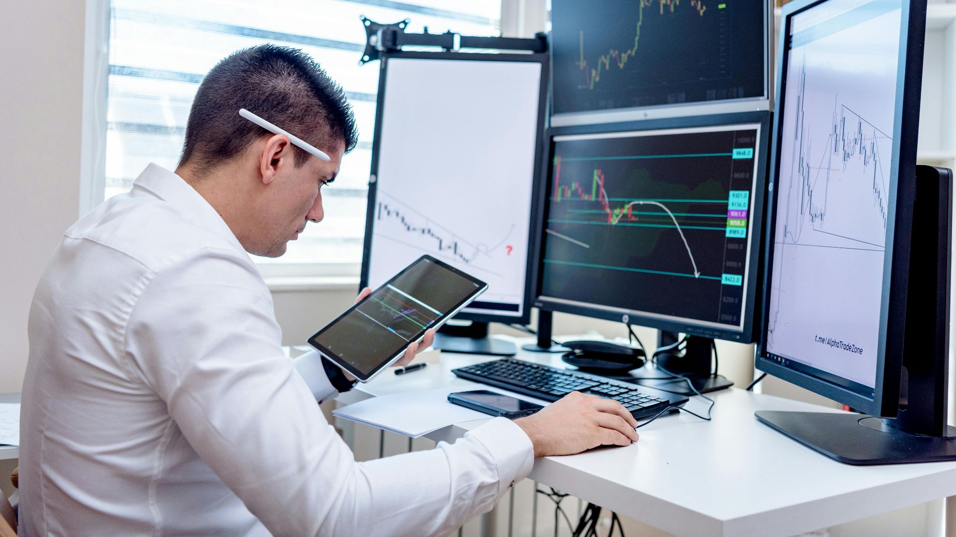 Professional analyzing stock market graphs on multiple monitors at work desk.