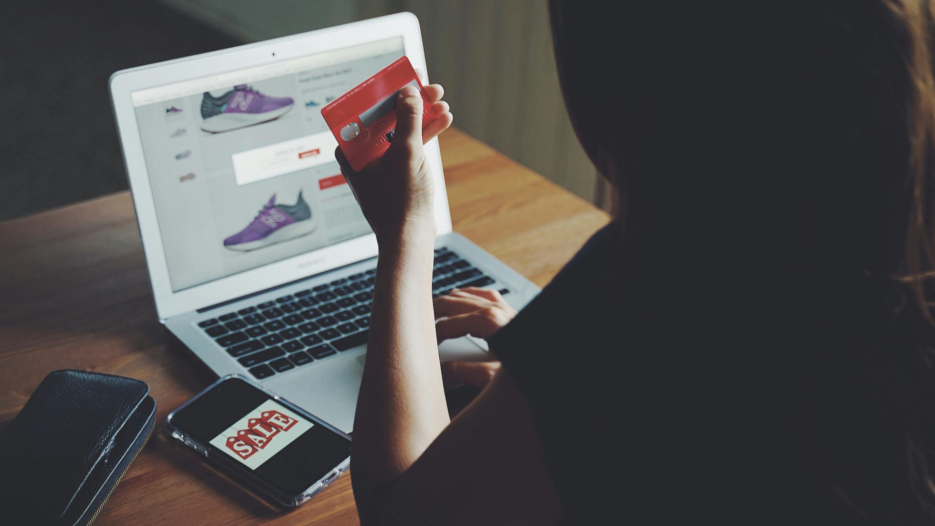 A woman shops online using a laptop and credit card on a wooden table.
