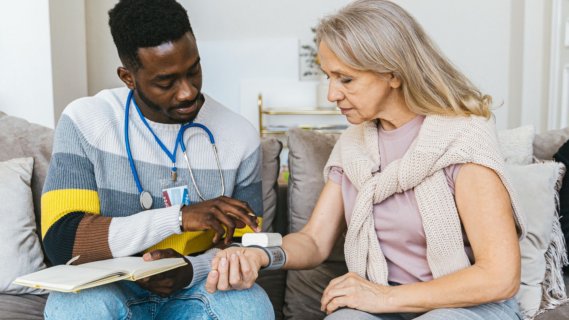 Healthcare professional checking blood pressure of elderly woman in a cozy indoor setting.