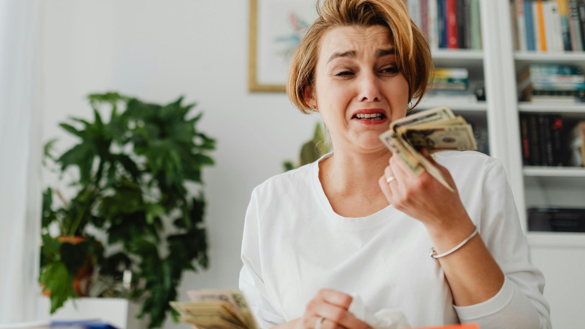 A woman looking stressed while counting money in a living room setting.
