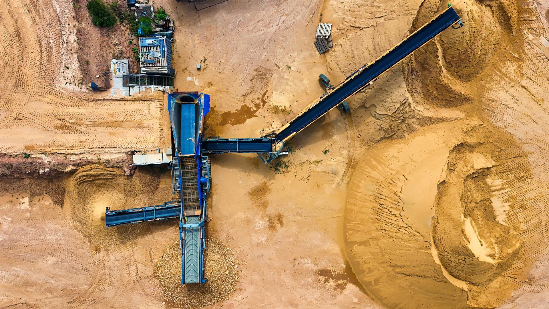 Top view of sand mining machinery and piles in outdoor quarry.