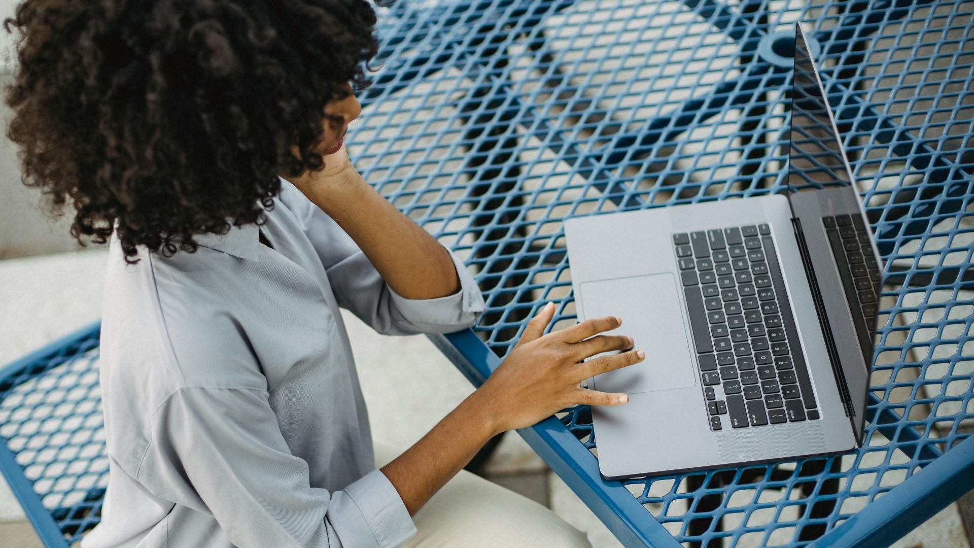 Woman with curly afro hair working on a laptop at an outdoor table, enjoying a relaxed day.