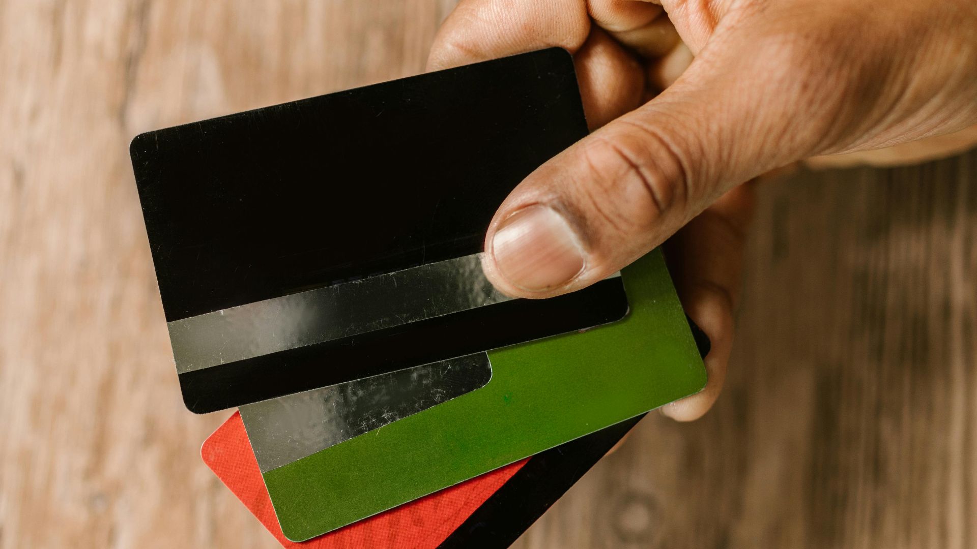 A hand holding multiple credit cards on a wooden background, emphasizing payment and finance themes.