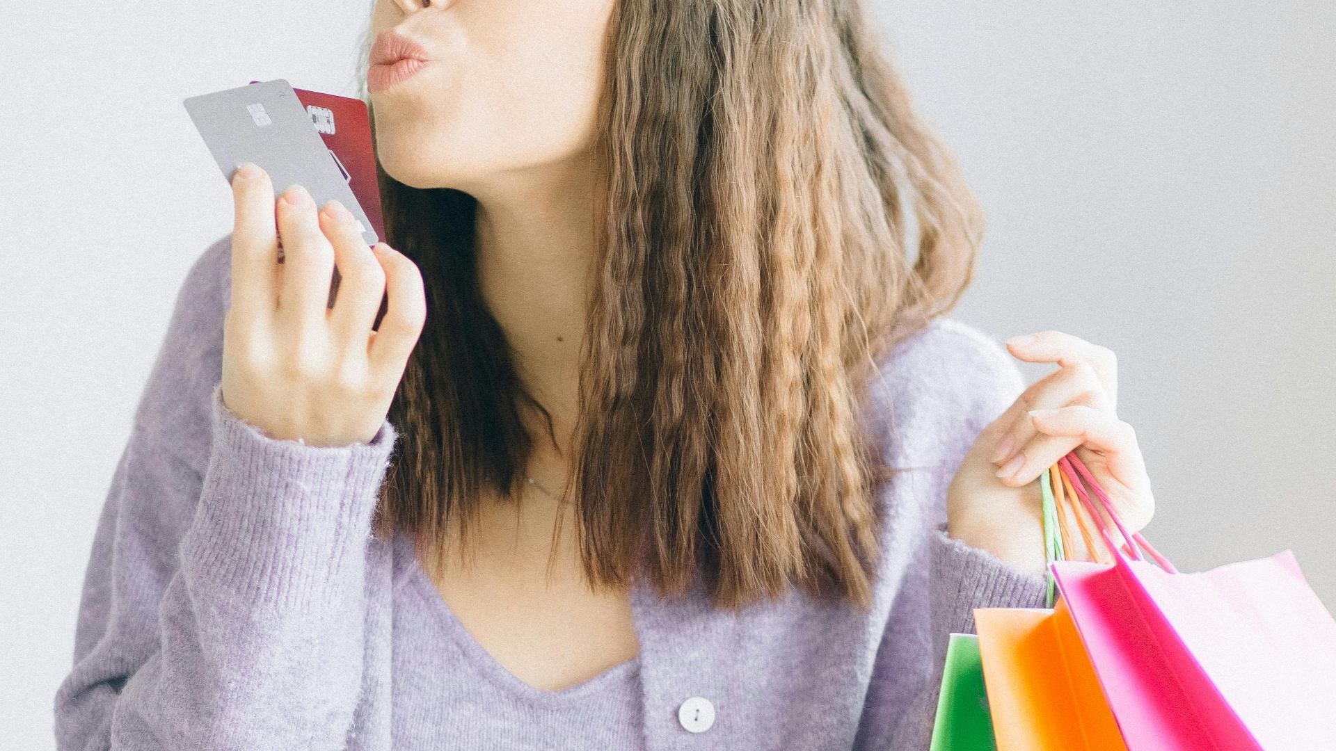 Woman playfully kissing credit card with colorful shopping bags in hand.