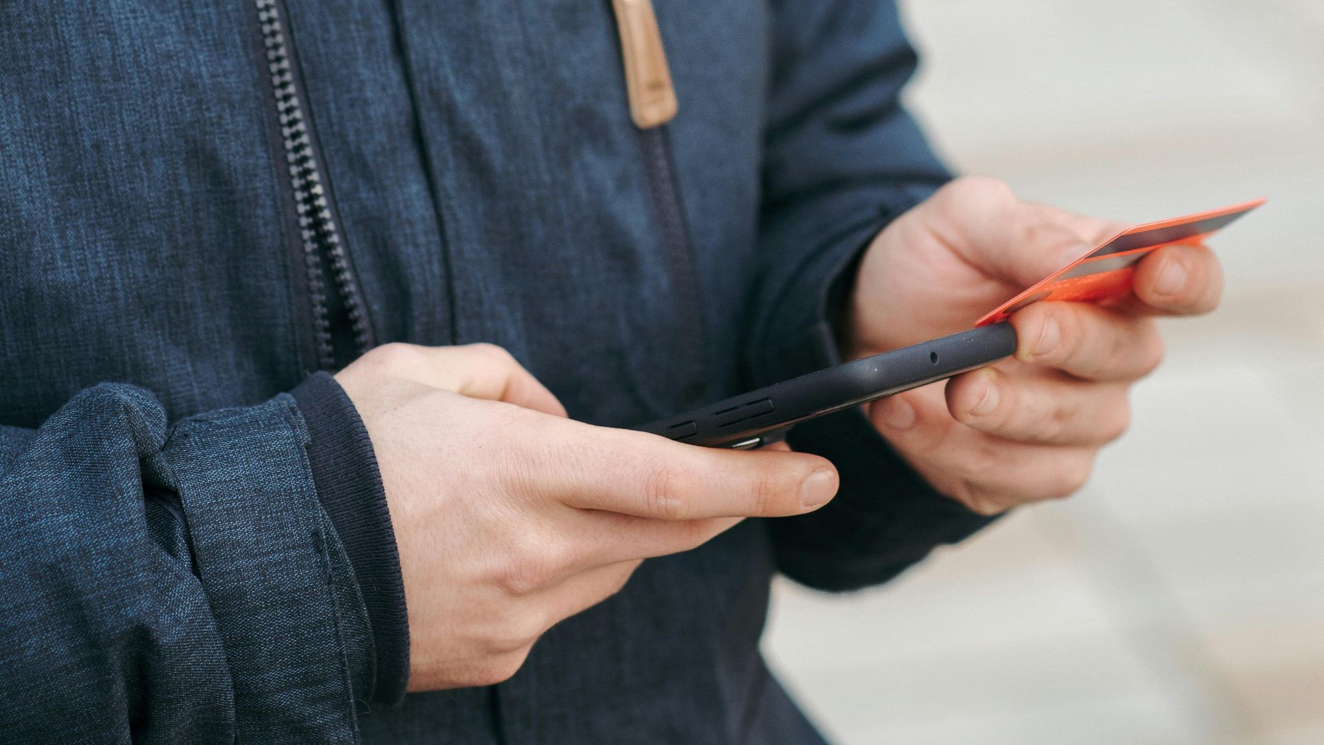 A young man using his smartphone and credit card outdoors for a transaction.