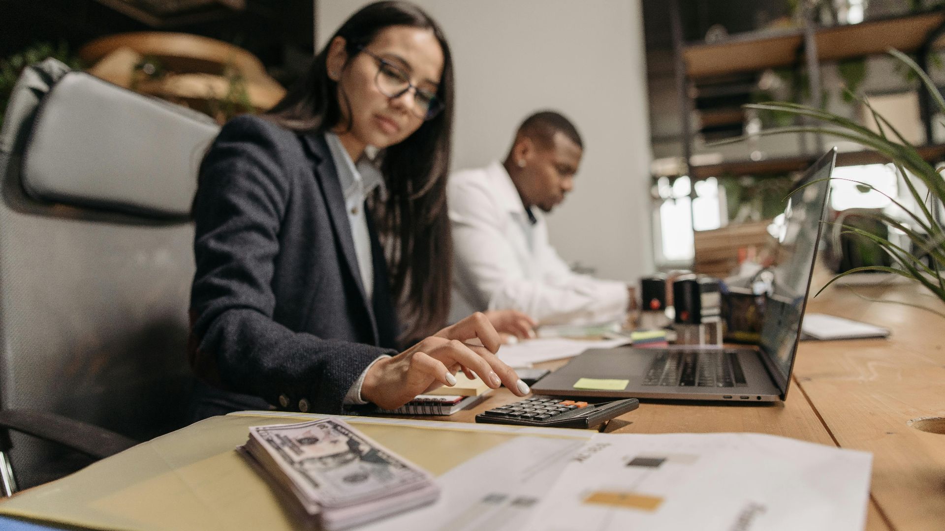 Two business professionals collaborating with a laptop and calculator in a modern office.