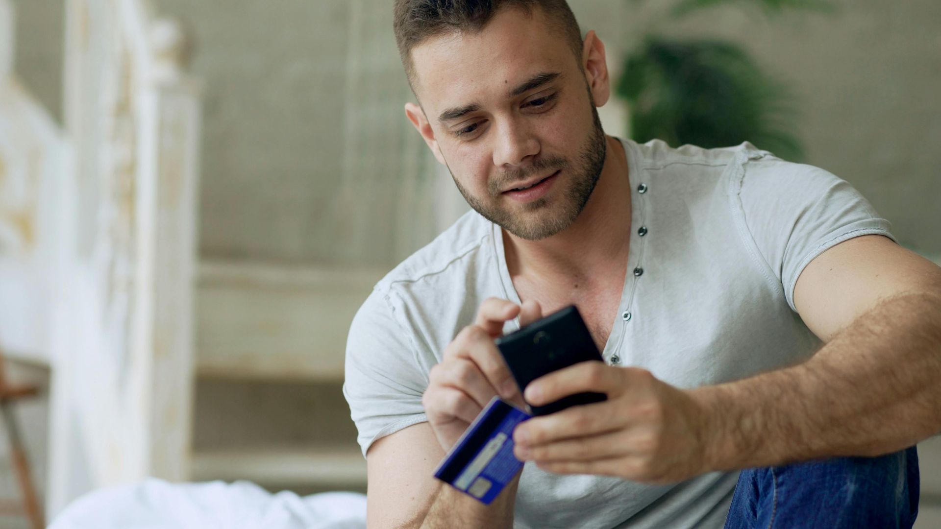 Young man using smartphone and credit card for online shopping indoors.