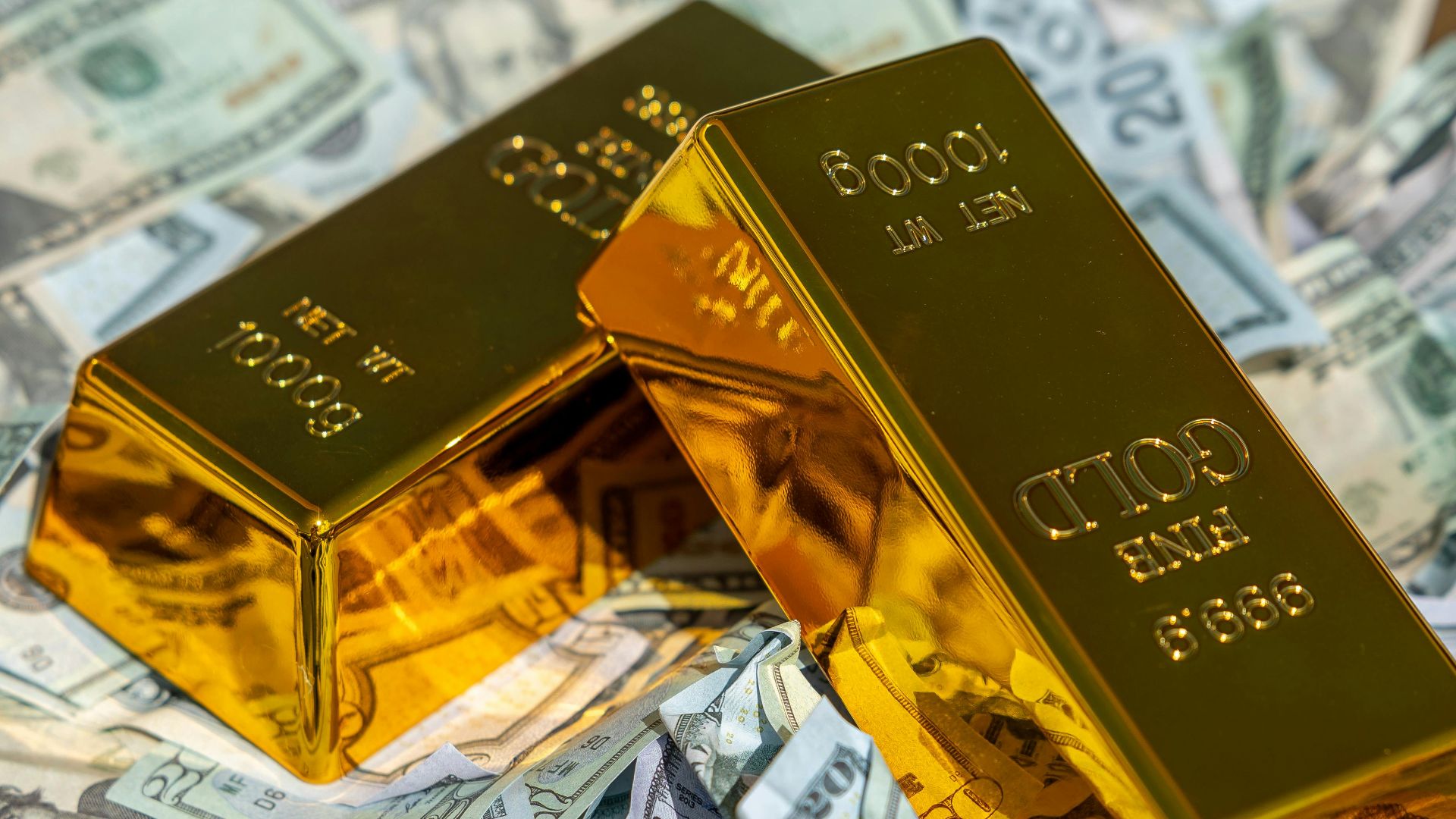 Two gold bars rest on a pile of US dollar bills, symbolizing wealth and prosperity.