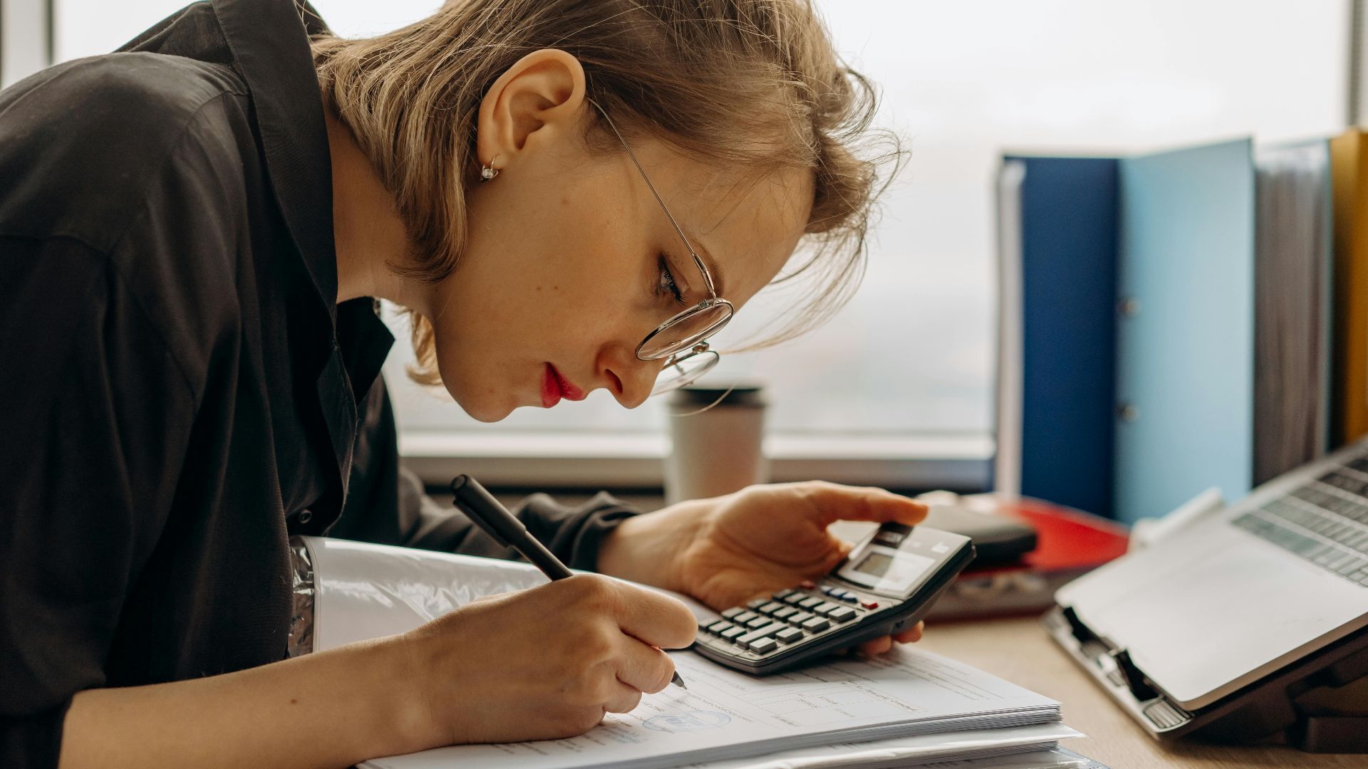 Young woman diligently working on accounting with a calculator and documents. Perfect for business and finance themes.