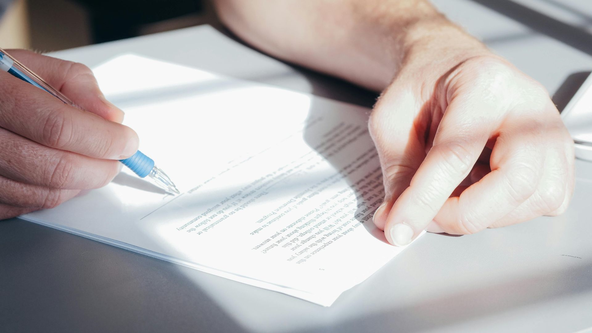 Hands signing a contract with a blue pen, close-up view.