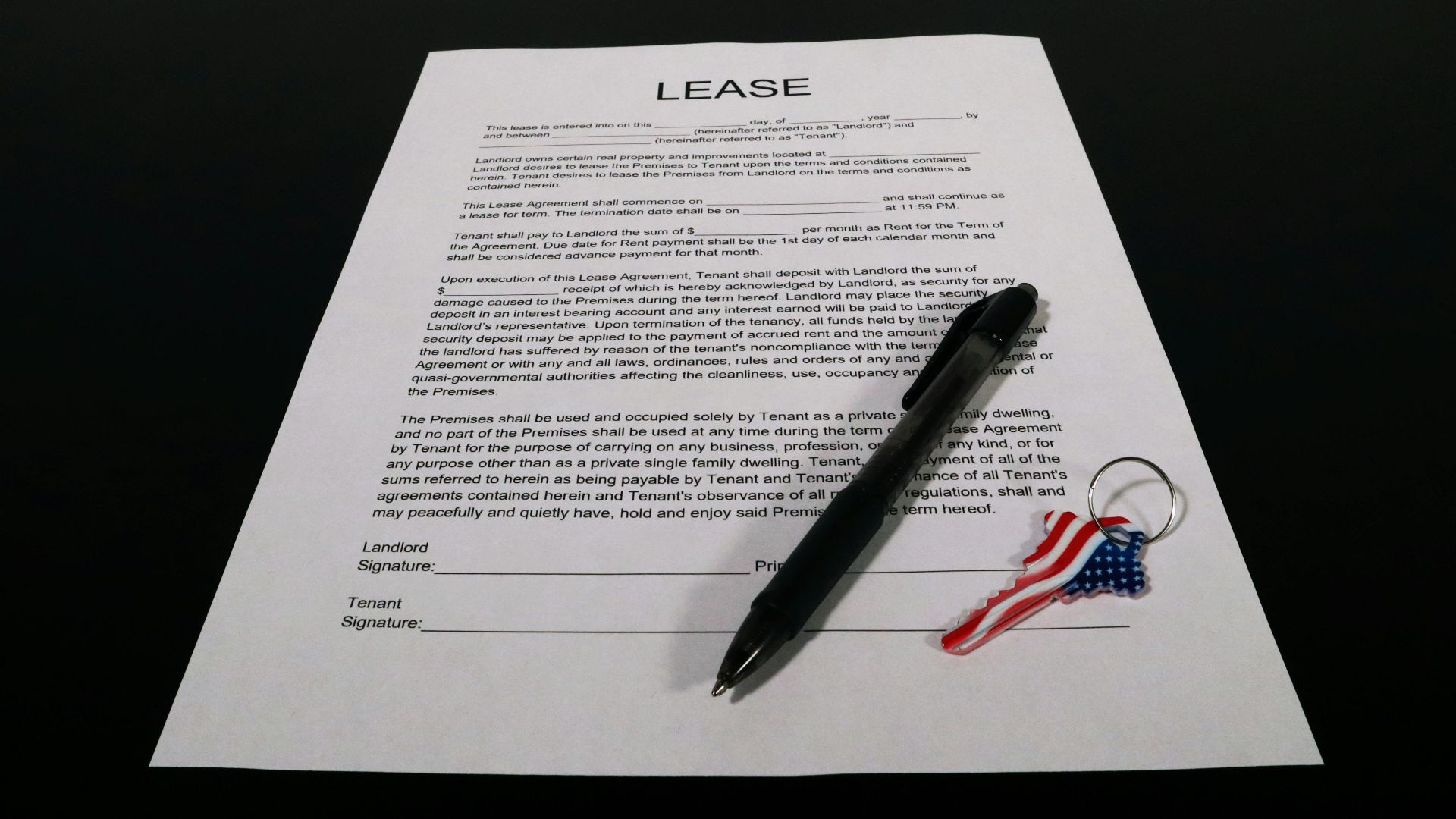 Lease agreement document with pen and American flag keychain on a black table.