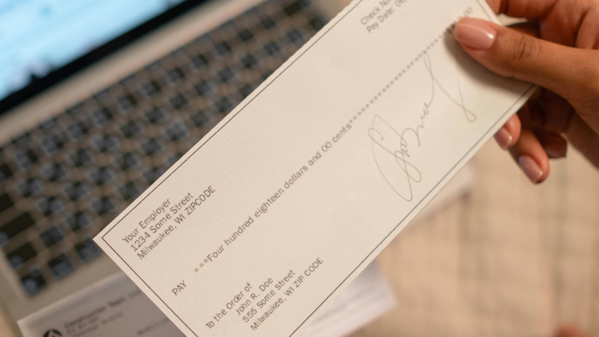 Individual holding a cheque over laptop, signifying online banking or financial transaction.