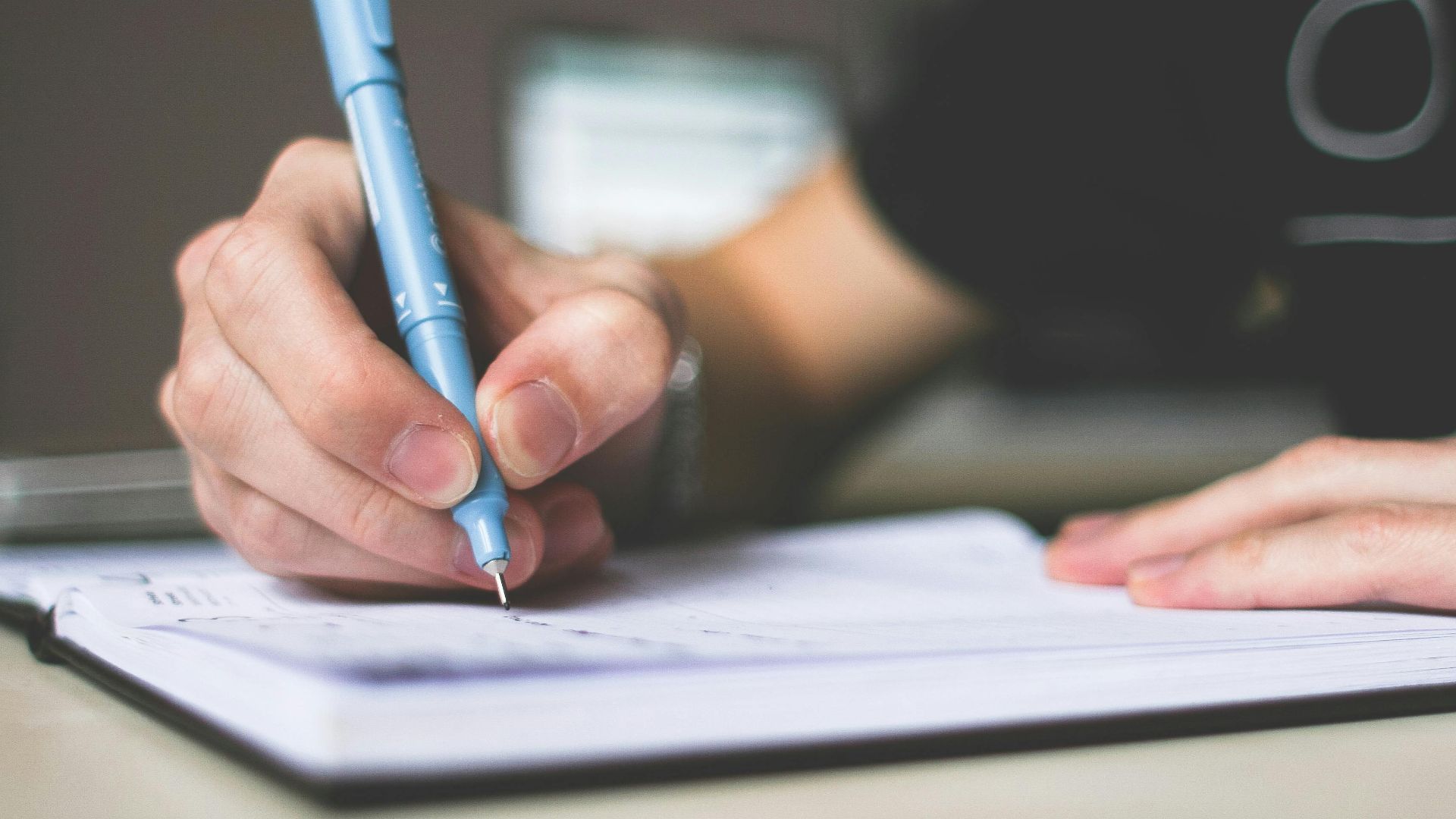 Close-up of hand writing in notebook using a blue pen, focus on creativity.