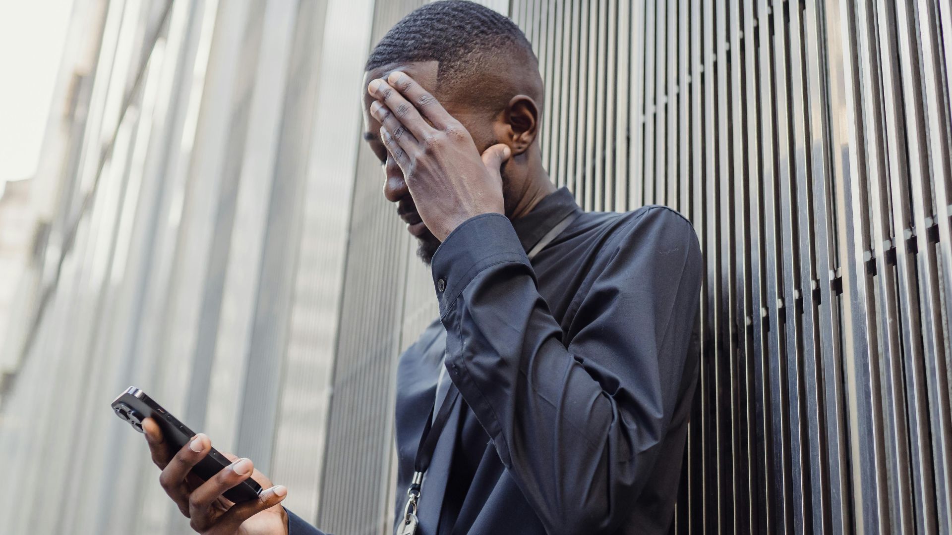 A worried businessman in formal attire using a smartphone outside a modern building.