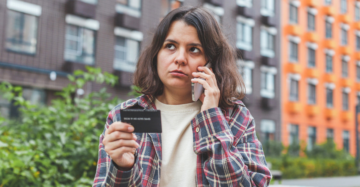 Woman standing outdoors, talking on the phone and holding a bank card