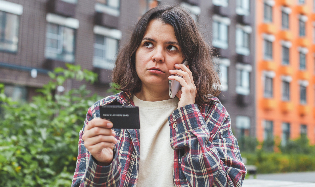 Woman standing outdoors, talking on the phone and holding a bank card