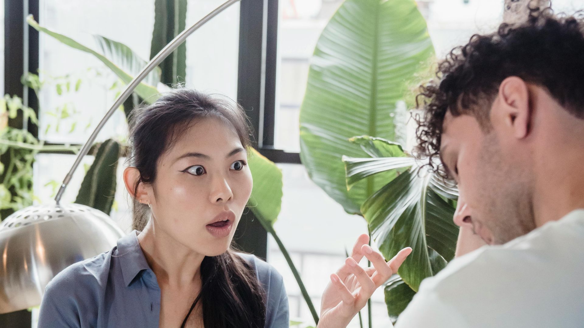A couple engaged in a heated discussion in a room with lush indoor plants.