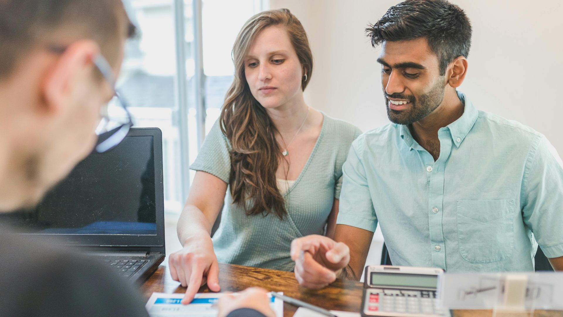 Young couple consulting with a financial advisor using a calculator and documents in a bright office setting.
