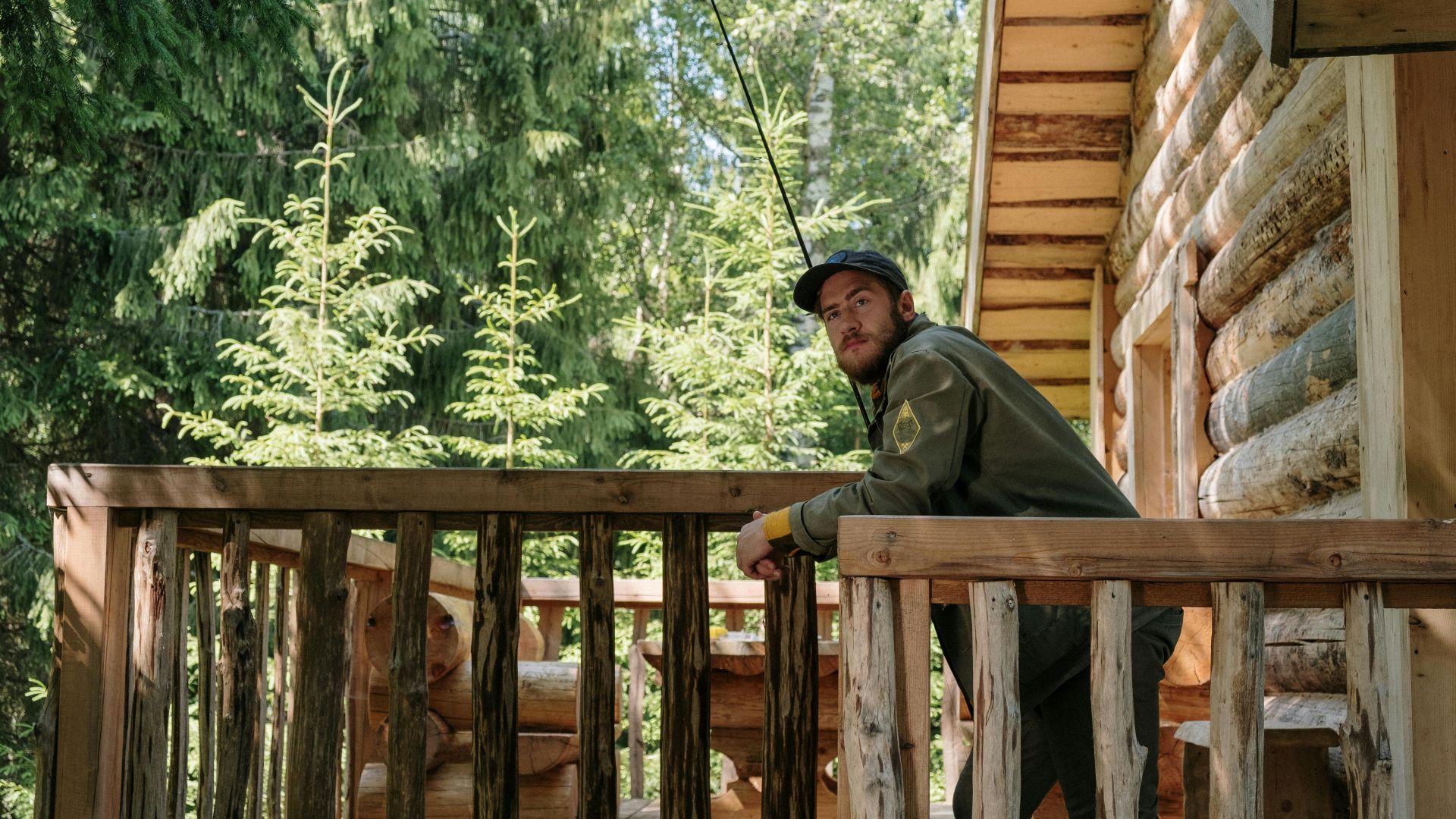 A man enjoying a peaceful fishing experience from a rustic wooden cabin terrace surrounded by lush greenery.