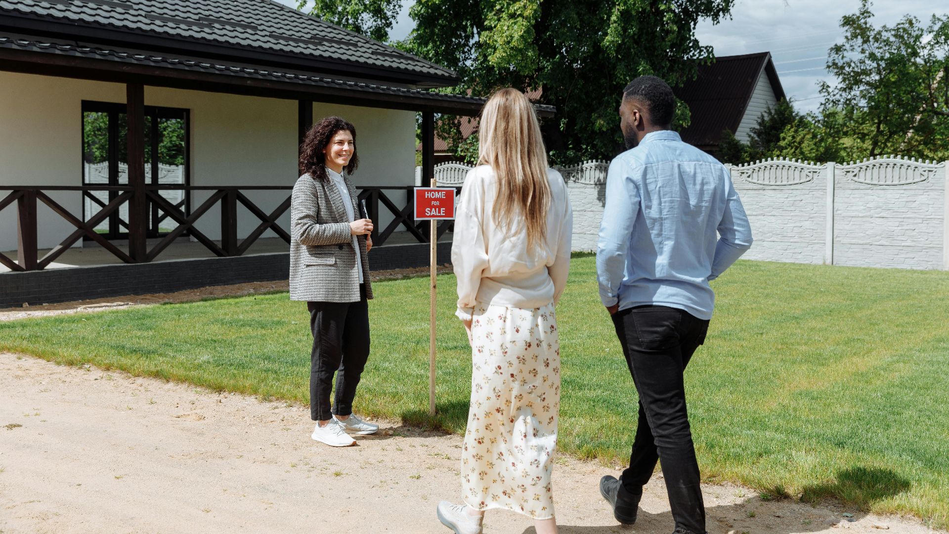 A diverse group viewing a house for sale with a real estate agent outdoors.