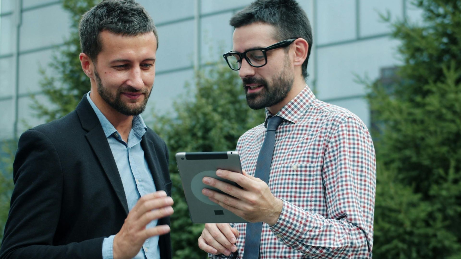 Two businessmen discussing work on a tablet in an outdoor setting.