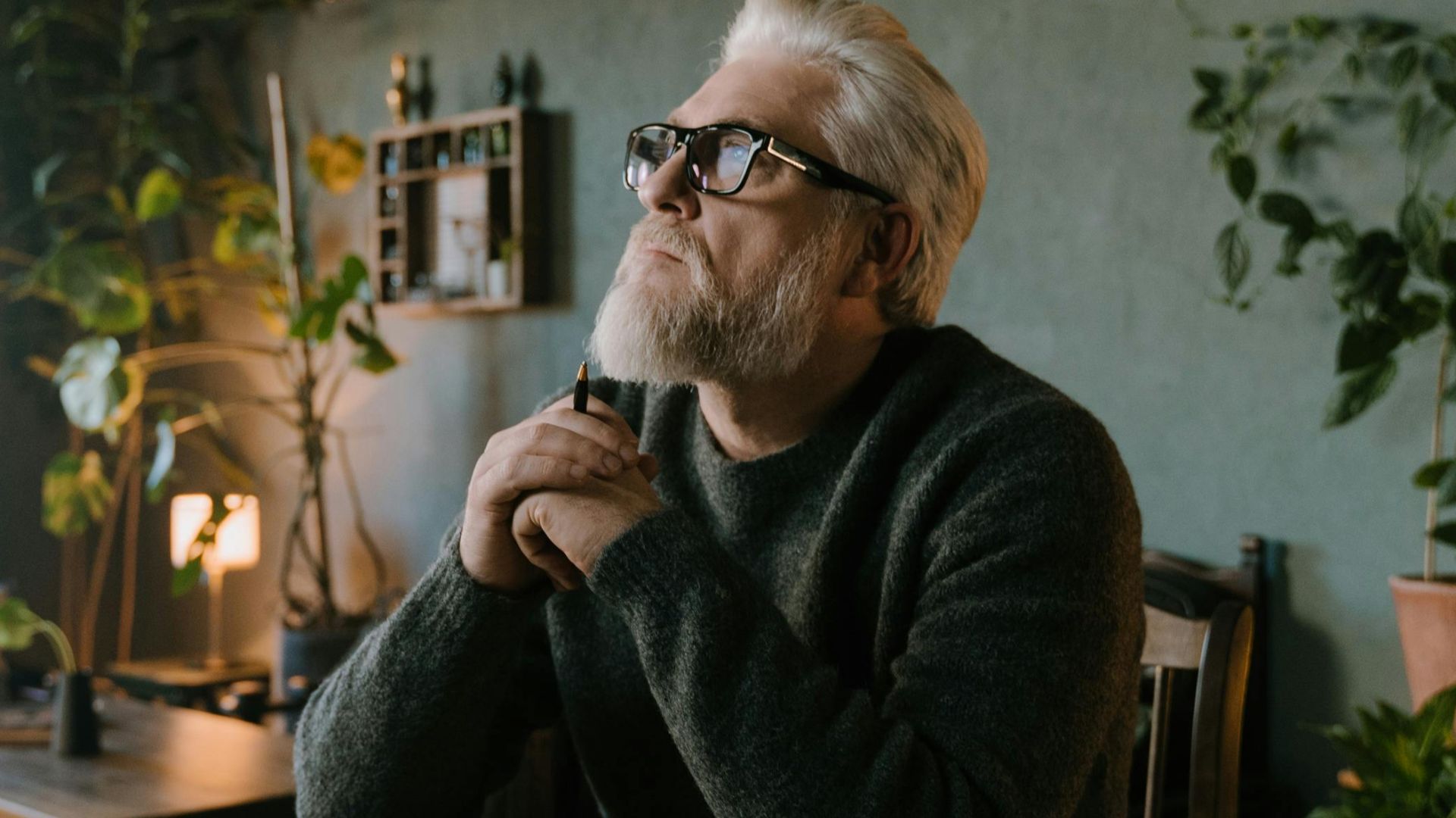 Senior man reflecting and writing at a cozy indoor setting with plants.