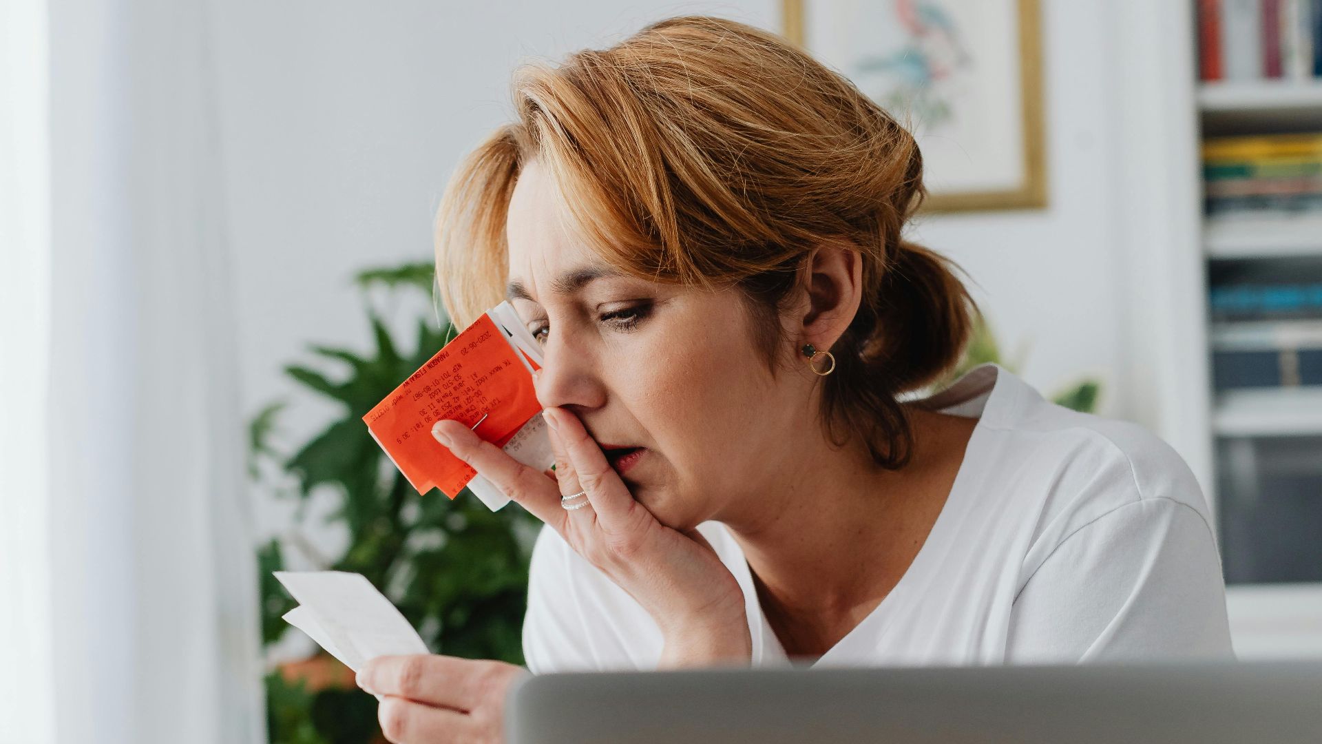 Woman concerned over finances with laptop, card, and receipts. Indoor, modern home office setting.