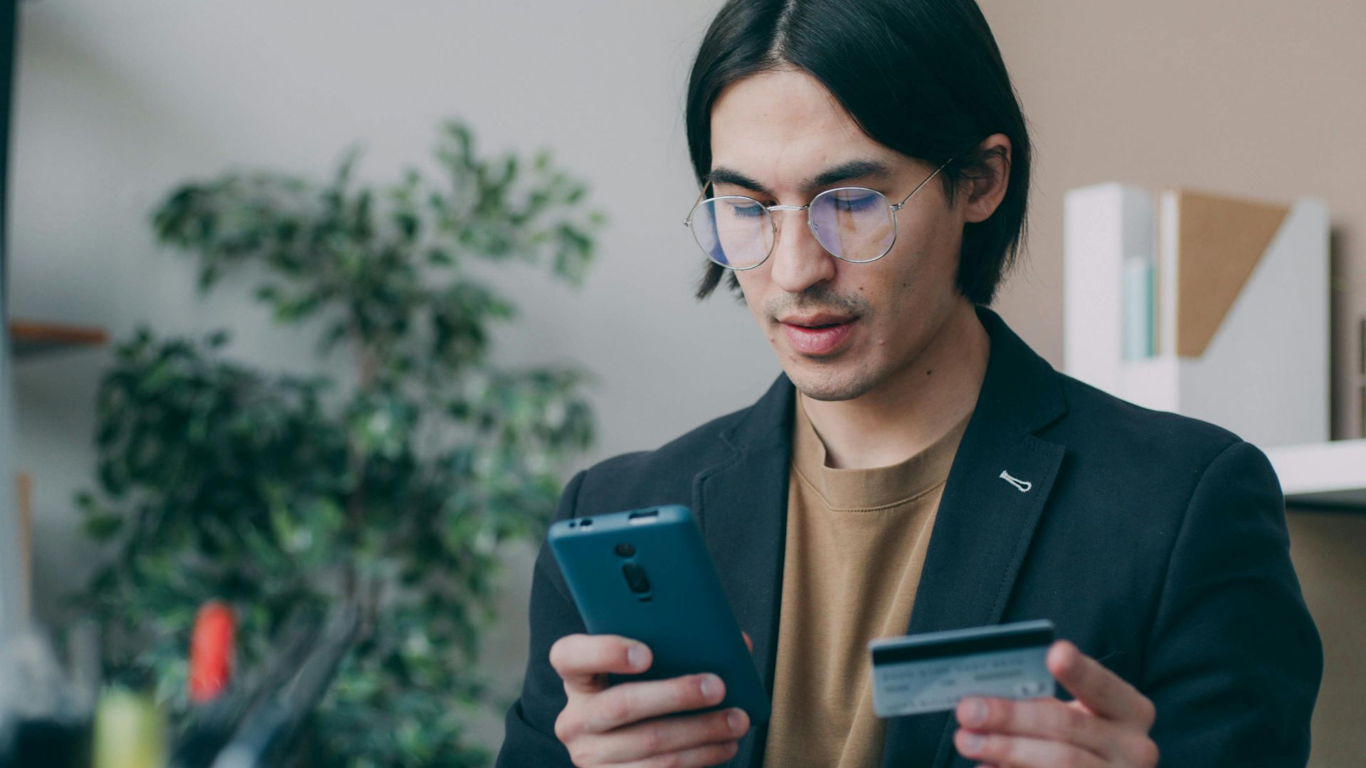Businessman in office attire using a smartphone and holding a credit card, focusing on online payment process.
