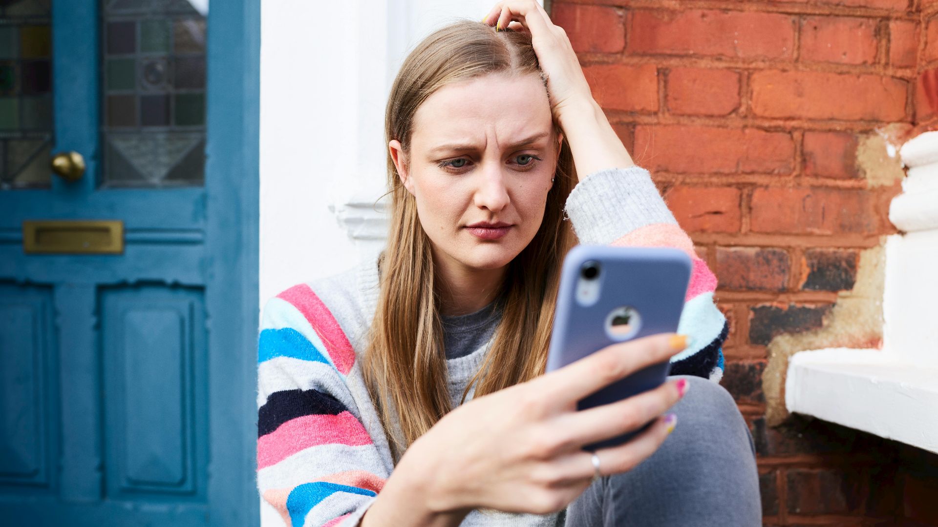 Young woman sitting outside a building, focused on her phone.