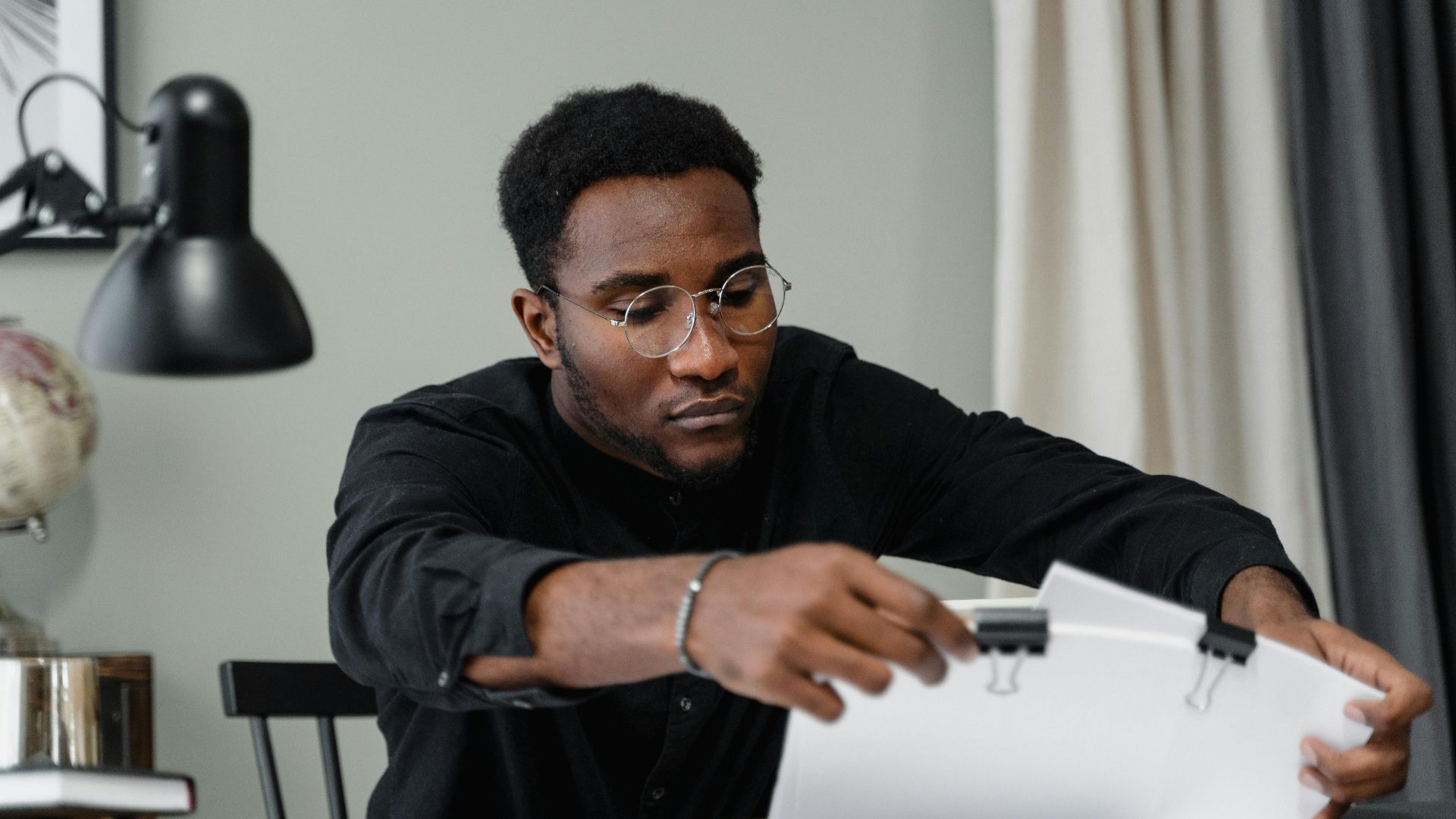 Professional man with glasses reviews documents at a desk in an office setting, emphasizing concentration.