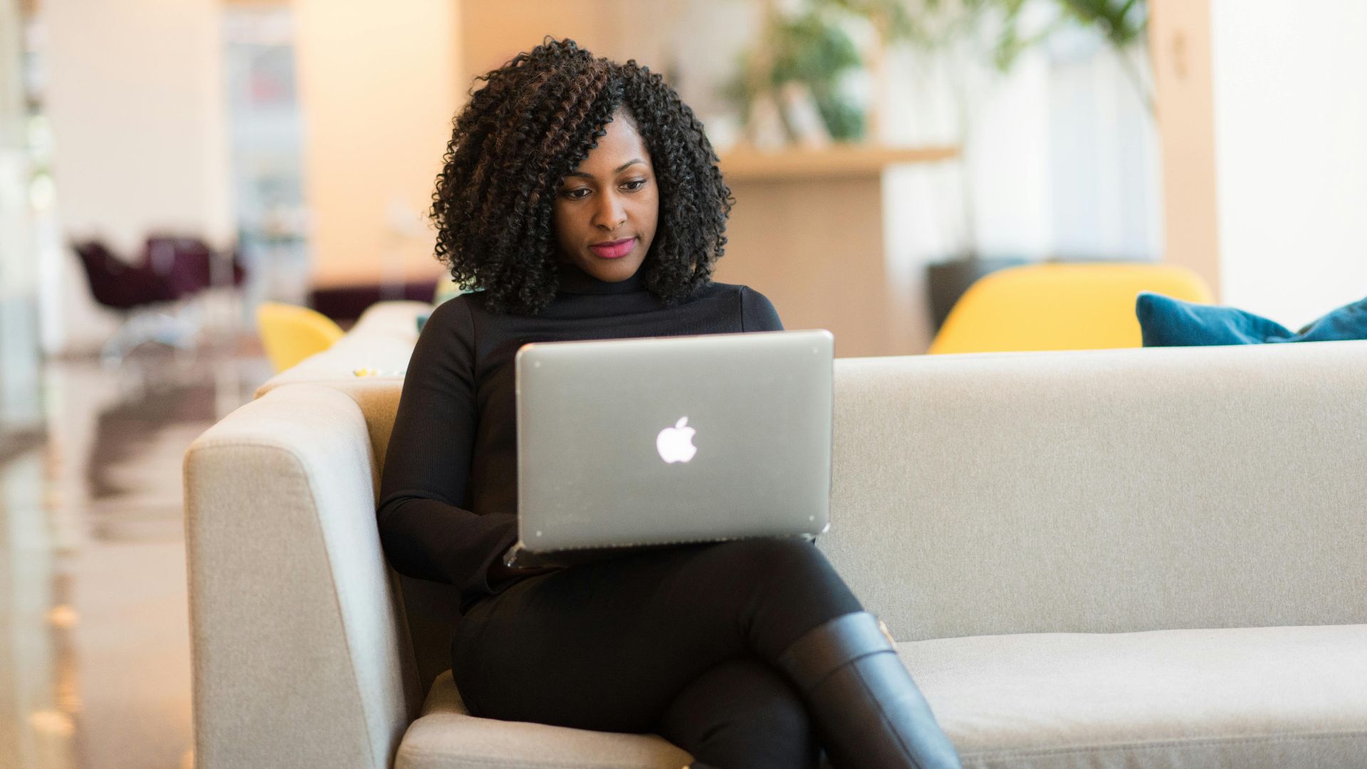 An African American woman working remotely on a laptop in a modern indoor setting.