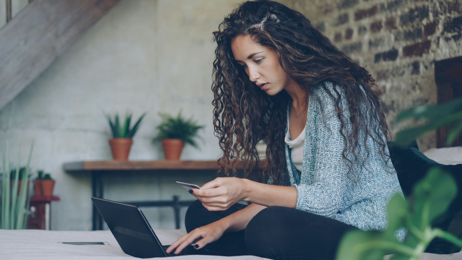 Woman using laptop and credit card on bed.