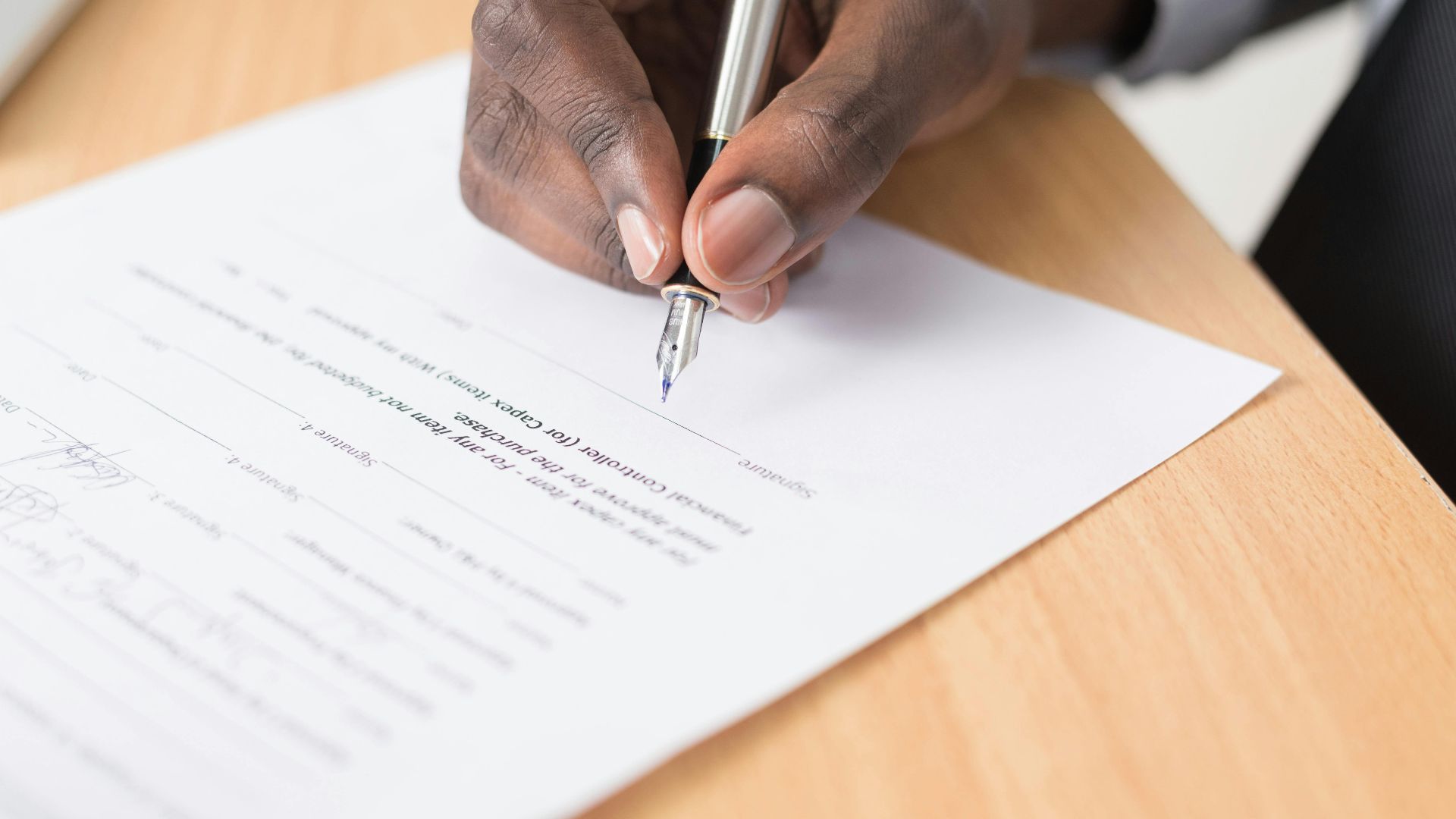 A hand holding a pen signing a document close-up on a desk, symbolizing agreement or contract finalization.