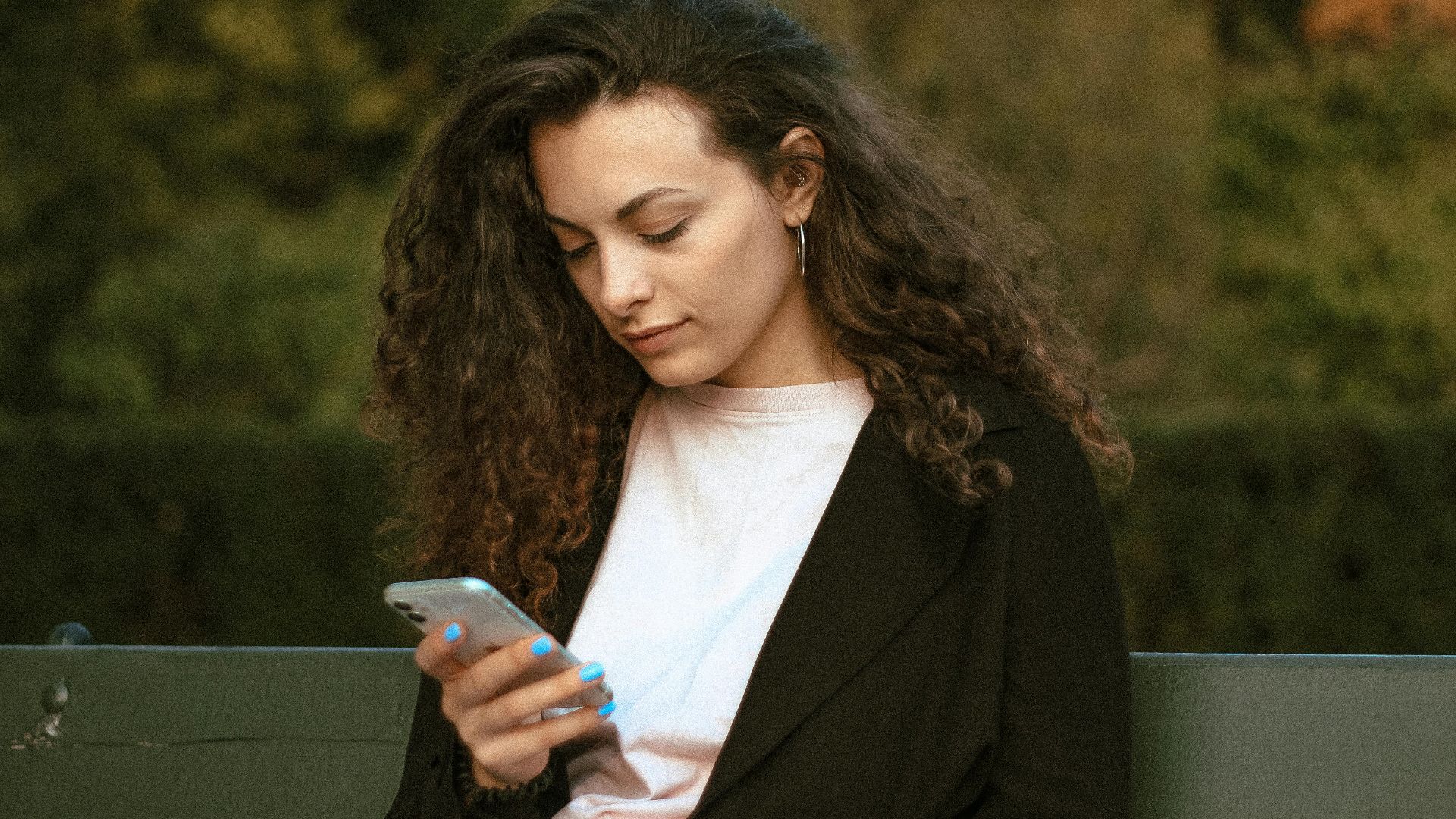 Woman with curly hair checking smartphone while sitting outdoors in Warsaw park.