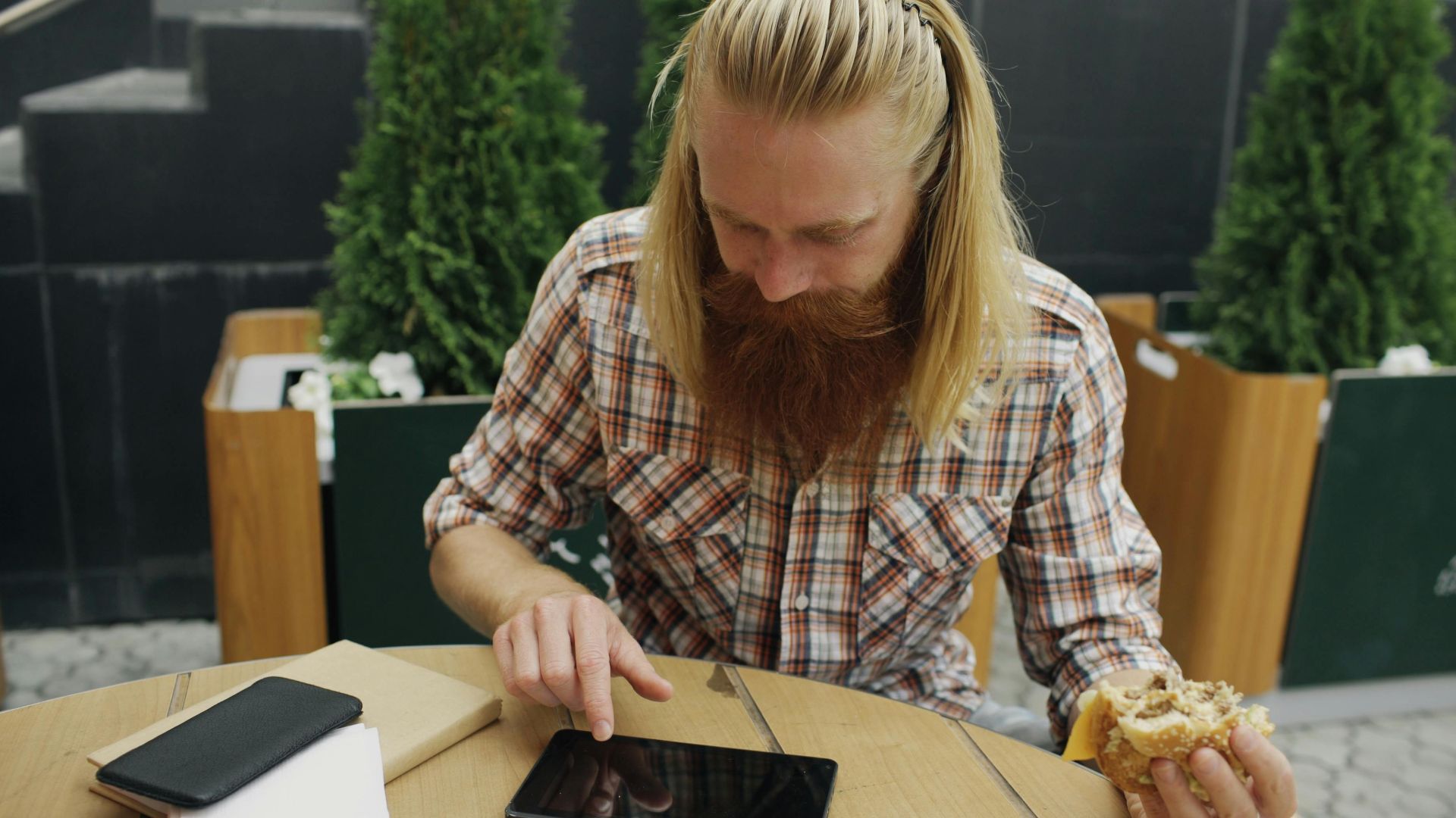 Bearded man using a tablet while having a coffee break at an outdoor cafe.