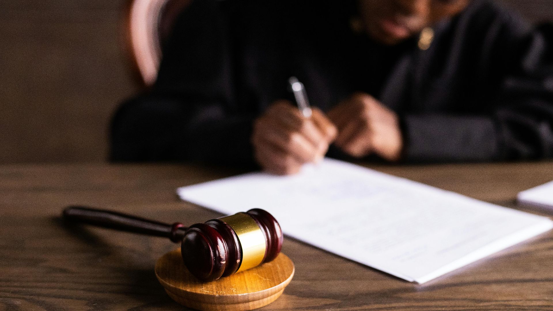 Judge signing documents at desk with focus on gavel, representing law and justice.