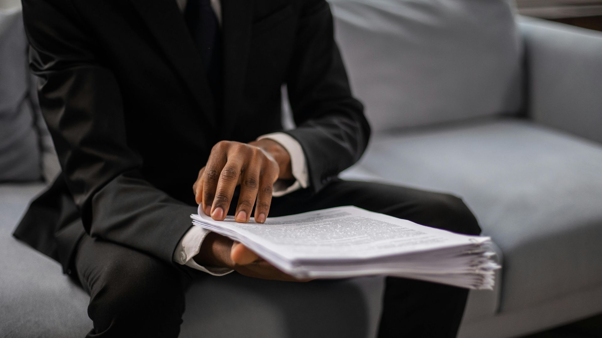 Close-up of a businessman in a suit reviewing documents while seated on a sofa indoors.