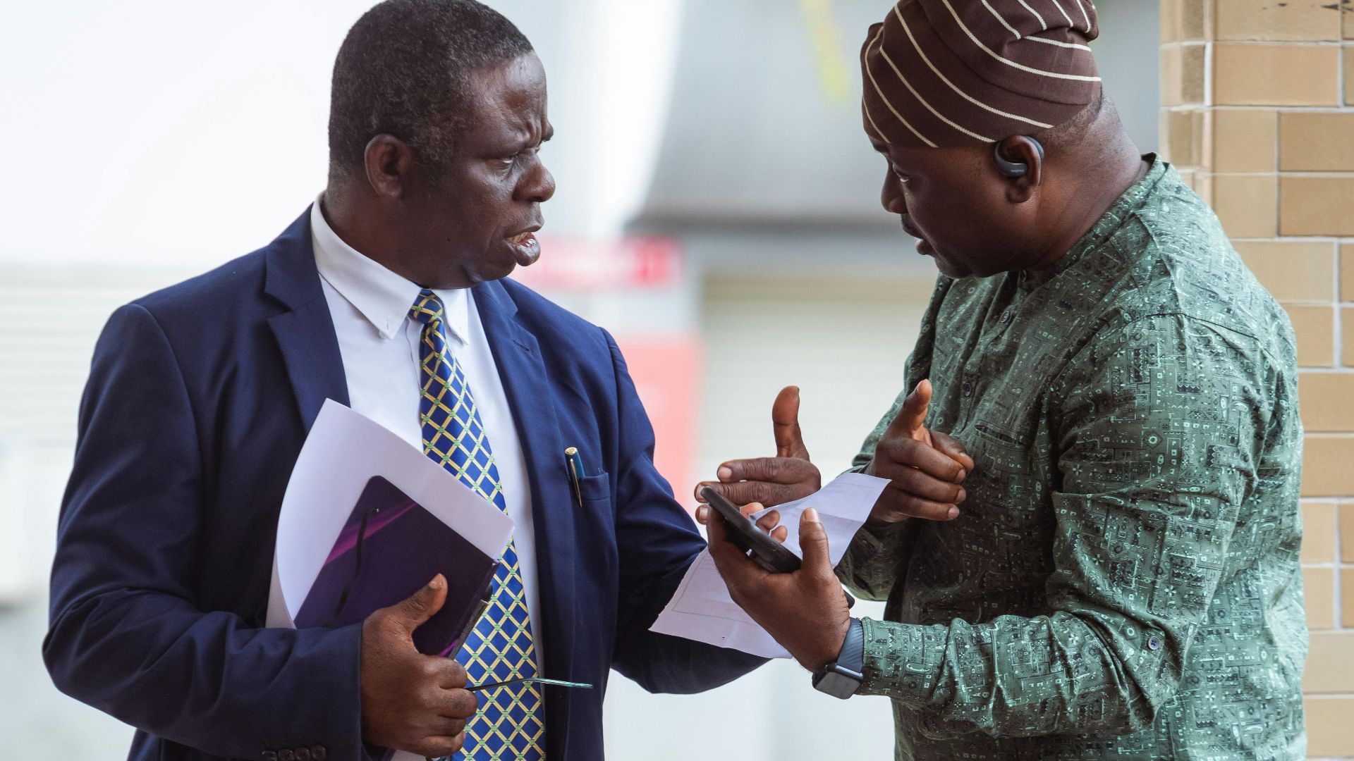 Two men engaged in a serious discussion outside, holding business documents.