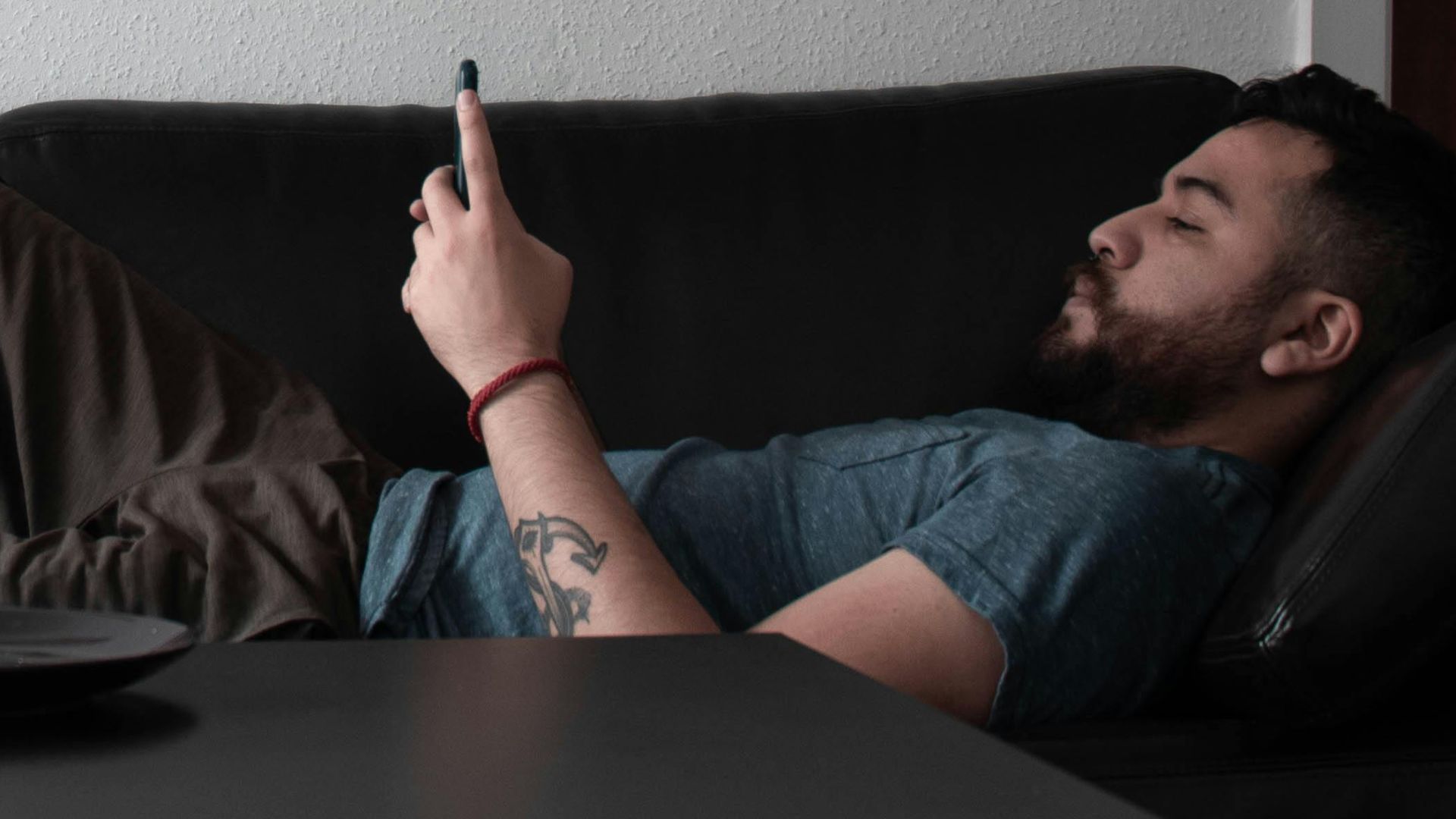 Adult man lying on a couch in a modern living room using a smartphone, relaxed atmosphere.