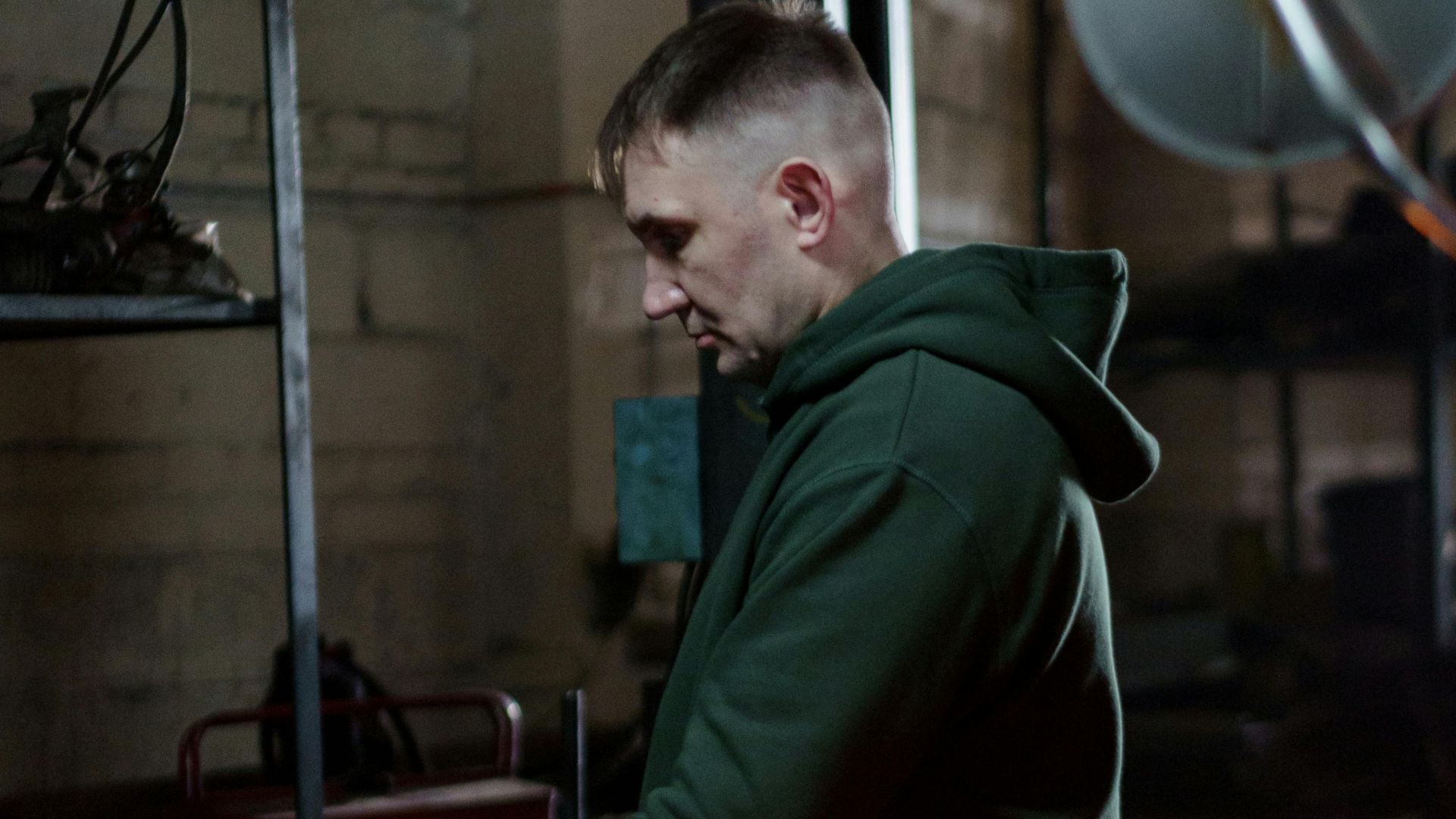 A focused mechanic working on automotive repair in a dimly lit garage setting.