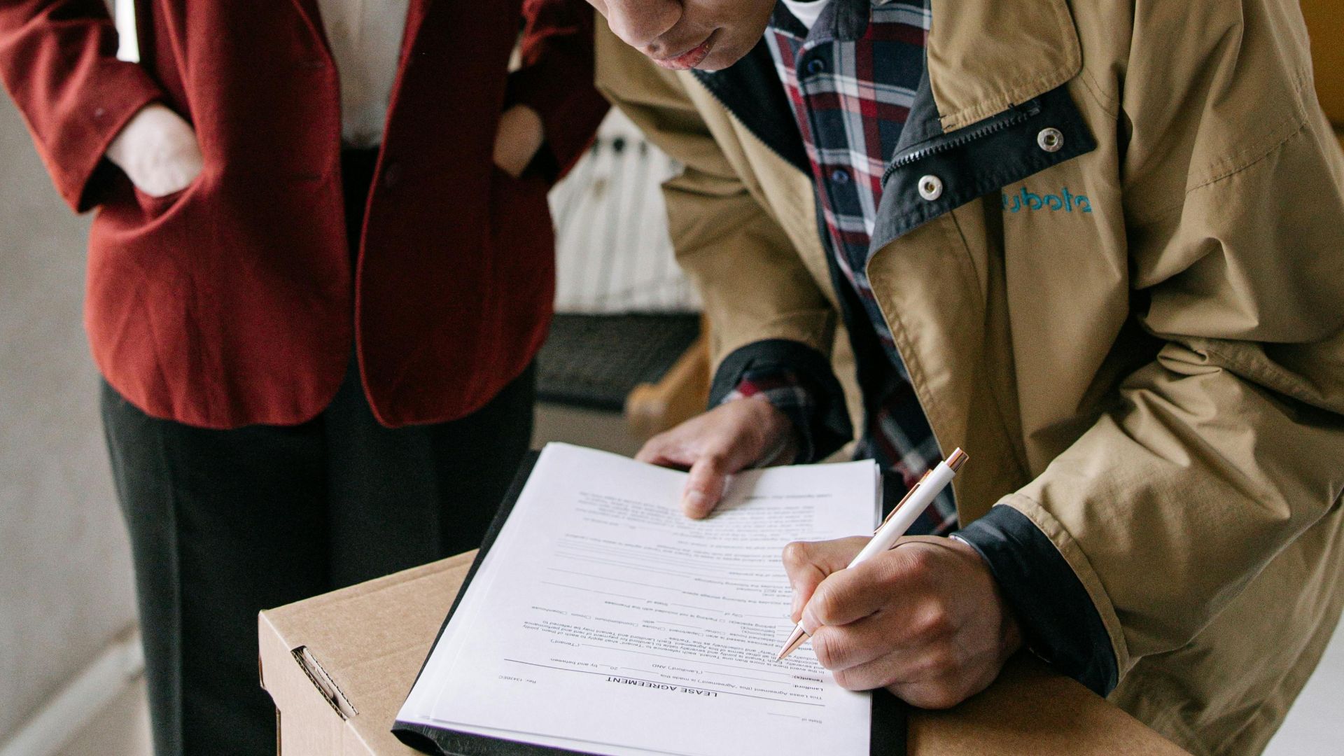 A young man signs a document while a woman observes, set in a modern office environment.