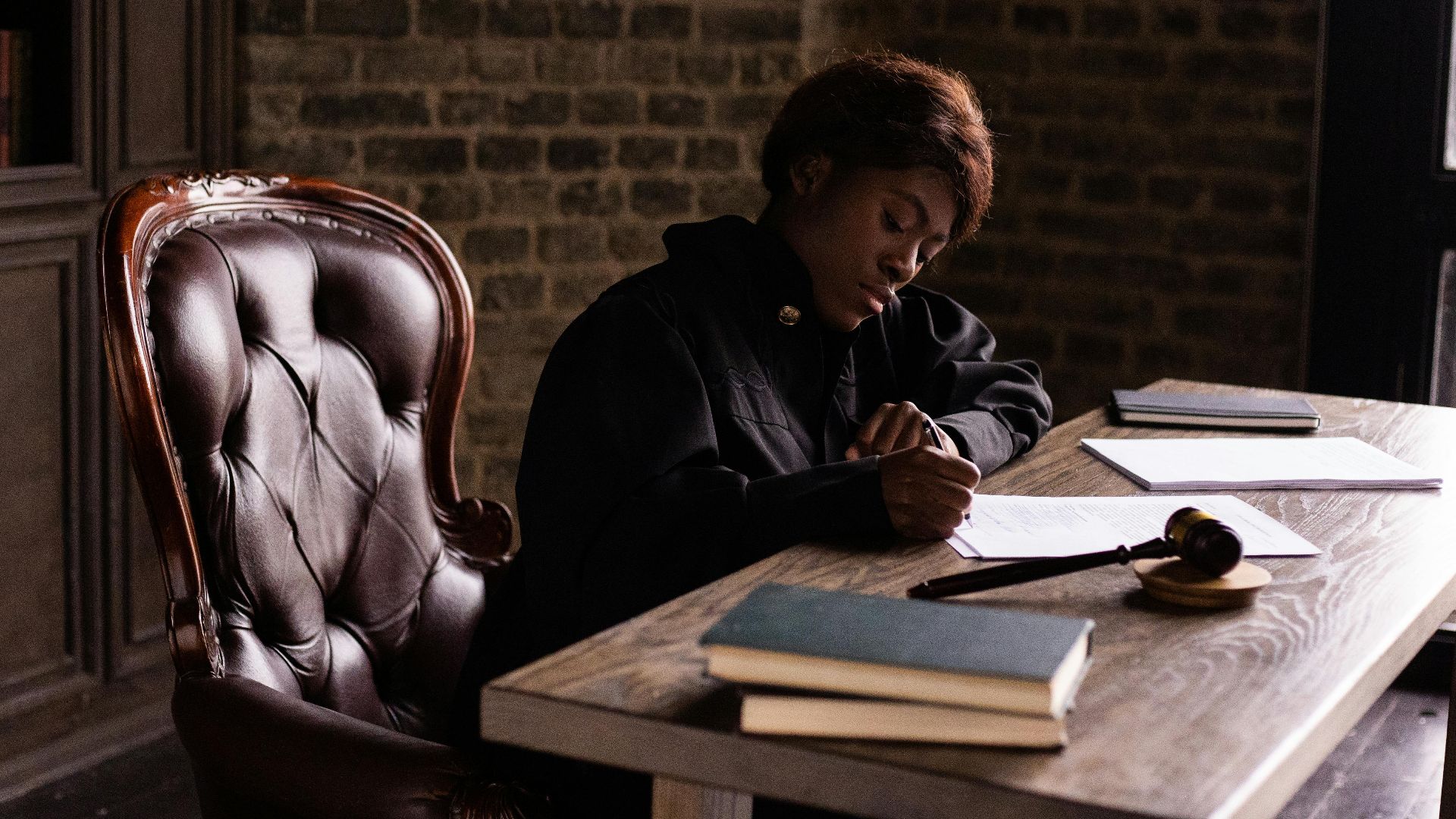 Black female judge in judicial robe writing at desk in an office setting, focusing on legal work.
