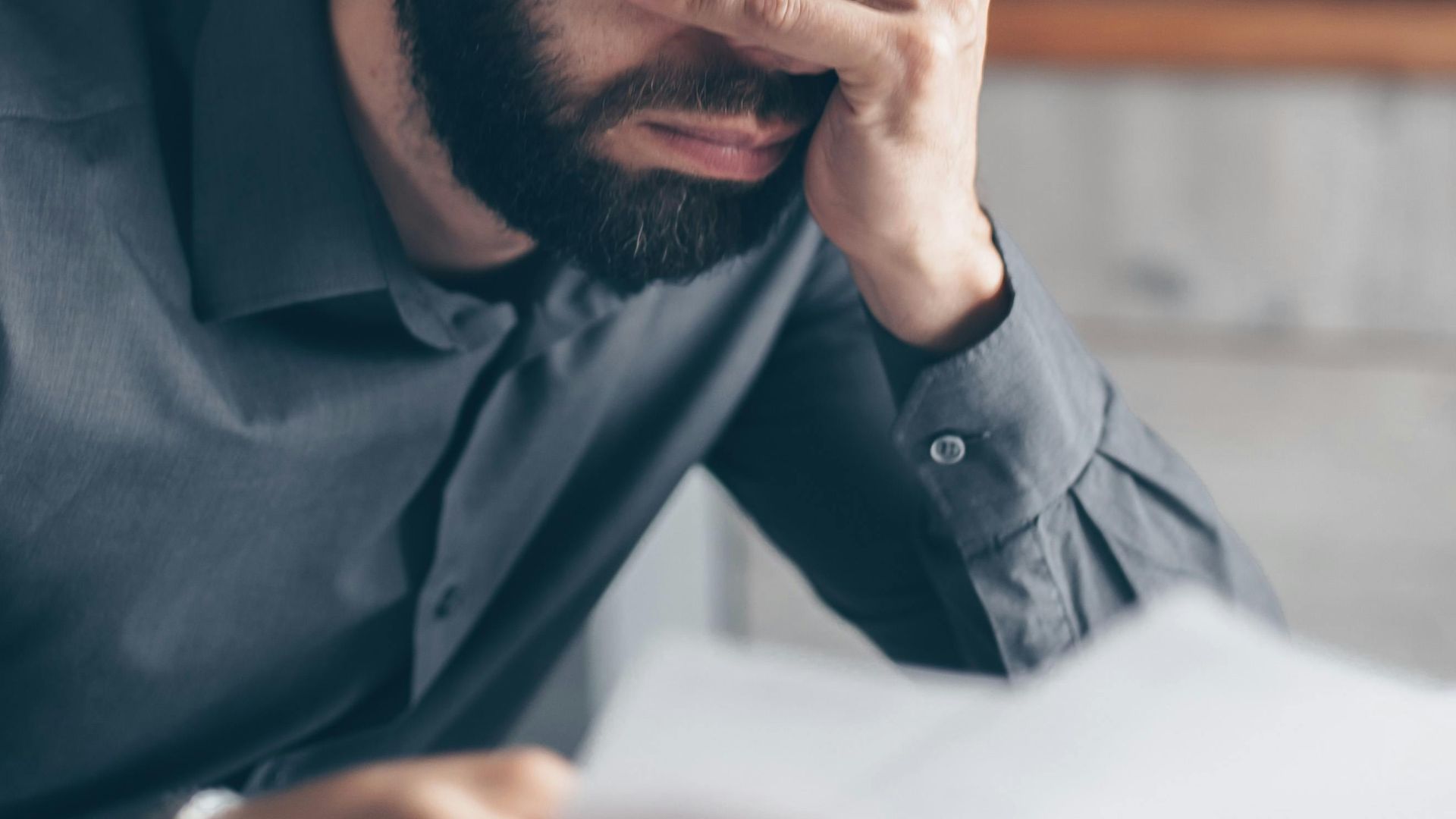 Man with glasses on head holds head in frustration while reading financial documents, indicating stress.