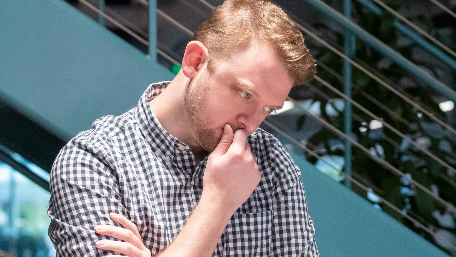 Man in a plaid shirt deep in thought while working in a modern office.